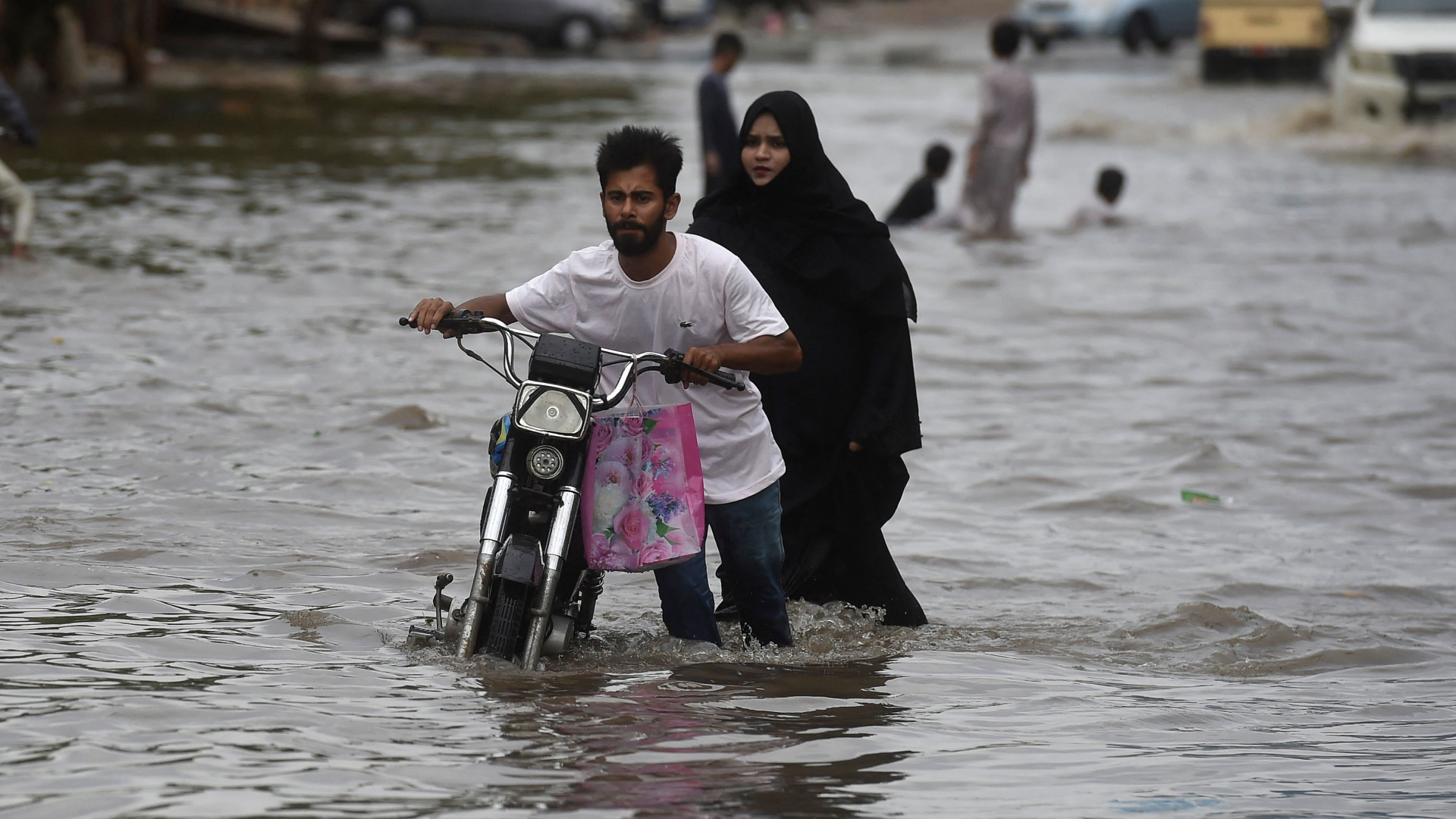 Ein Mann schiebt sein Motorrad auf einer überfluteten Straße in Karachi in Pakistan. | AFP