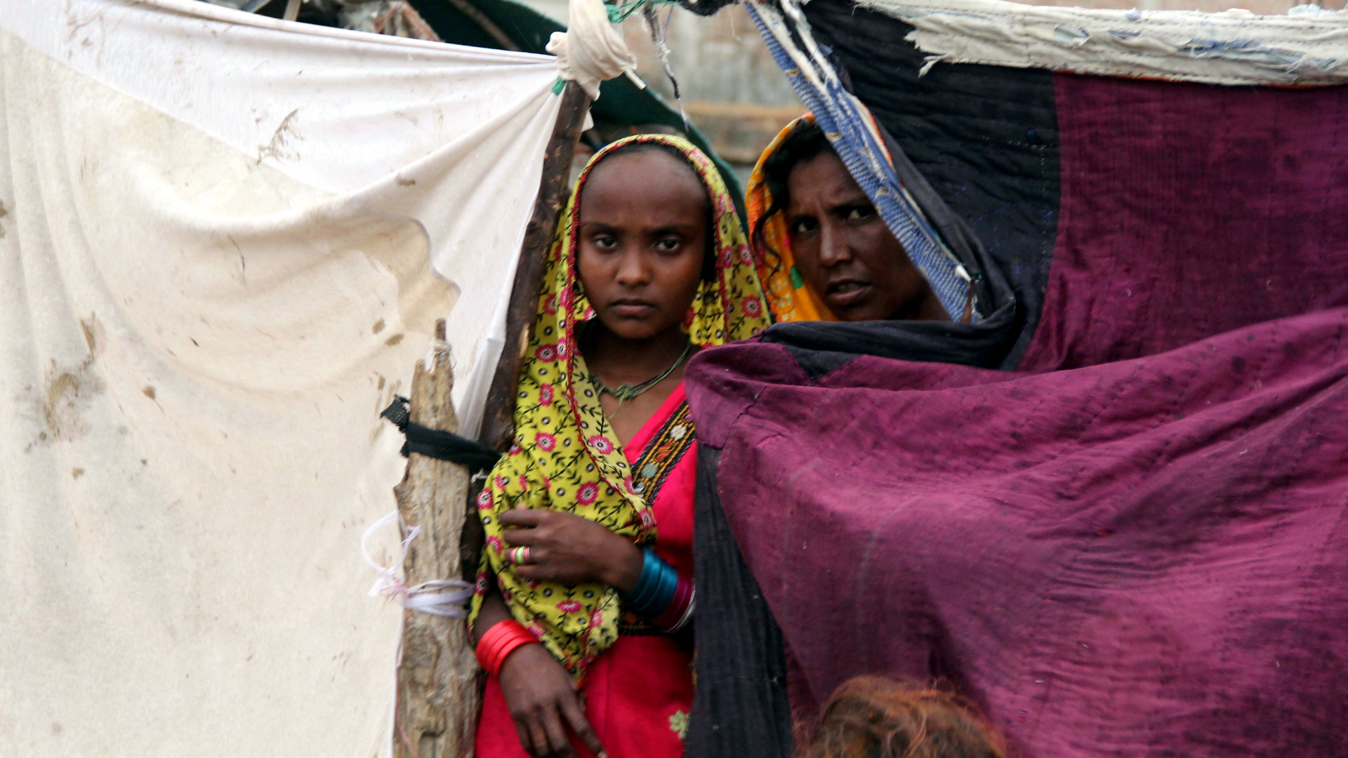 Zwei Frauen schauen hinter der Zeltplane ihrer notdürftig errichteten Unterkunft nahe Hyderabad in der Provinz Sindh hervor.