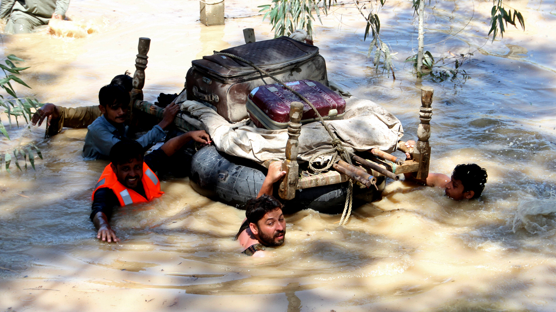 Vertriebene tragen am Stadtrand von Peschawar, Pakistan, Habseligkeiten, die aus von Überschwemmungen betroffenen Häusern geborgen wurden, durch ein überschwemmtes Gebiet.