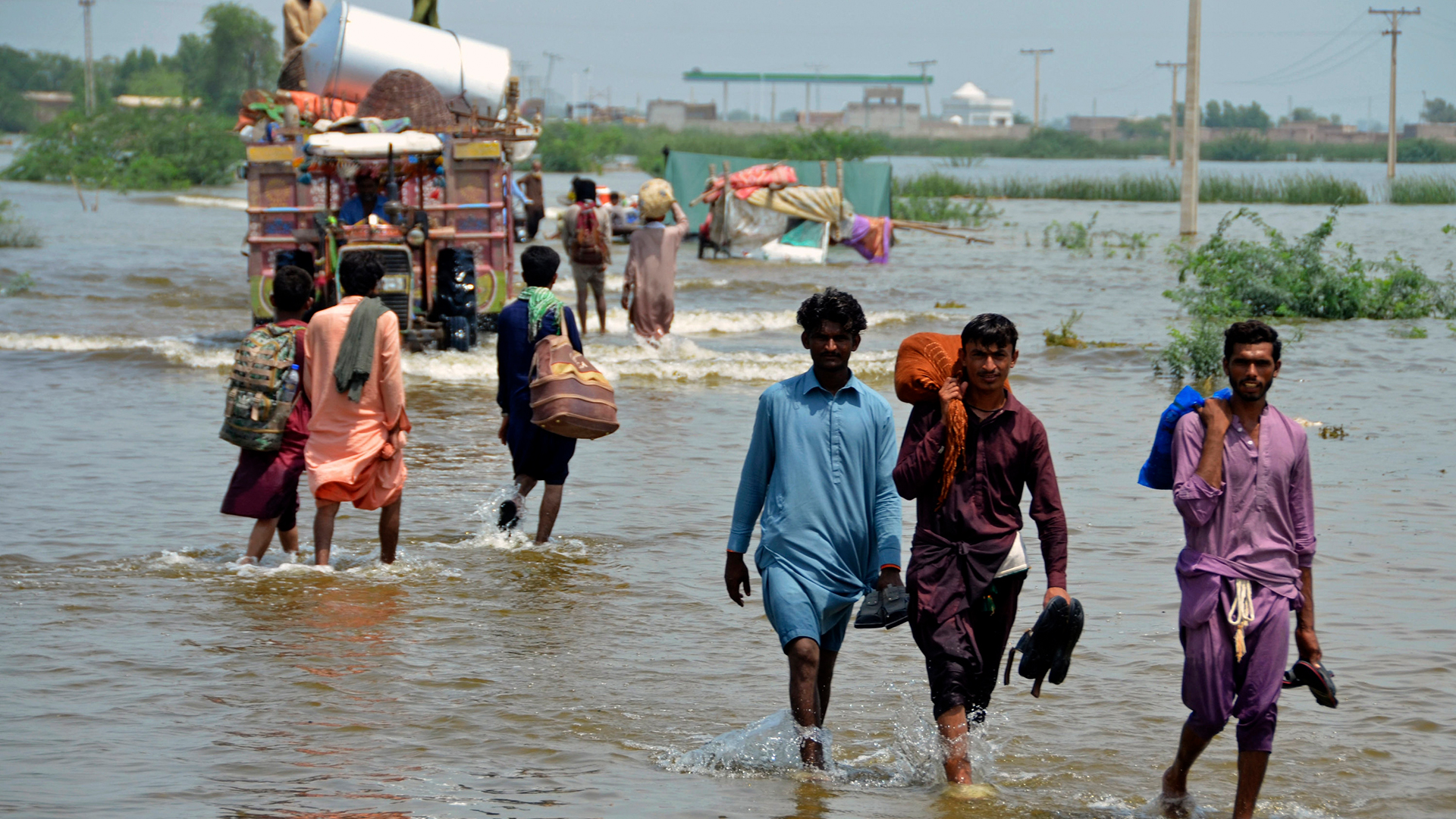 Menschen gehen über ein überschwemmtes Gebiet in Pakistan. | AP