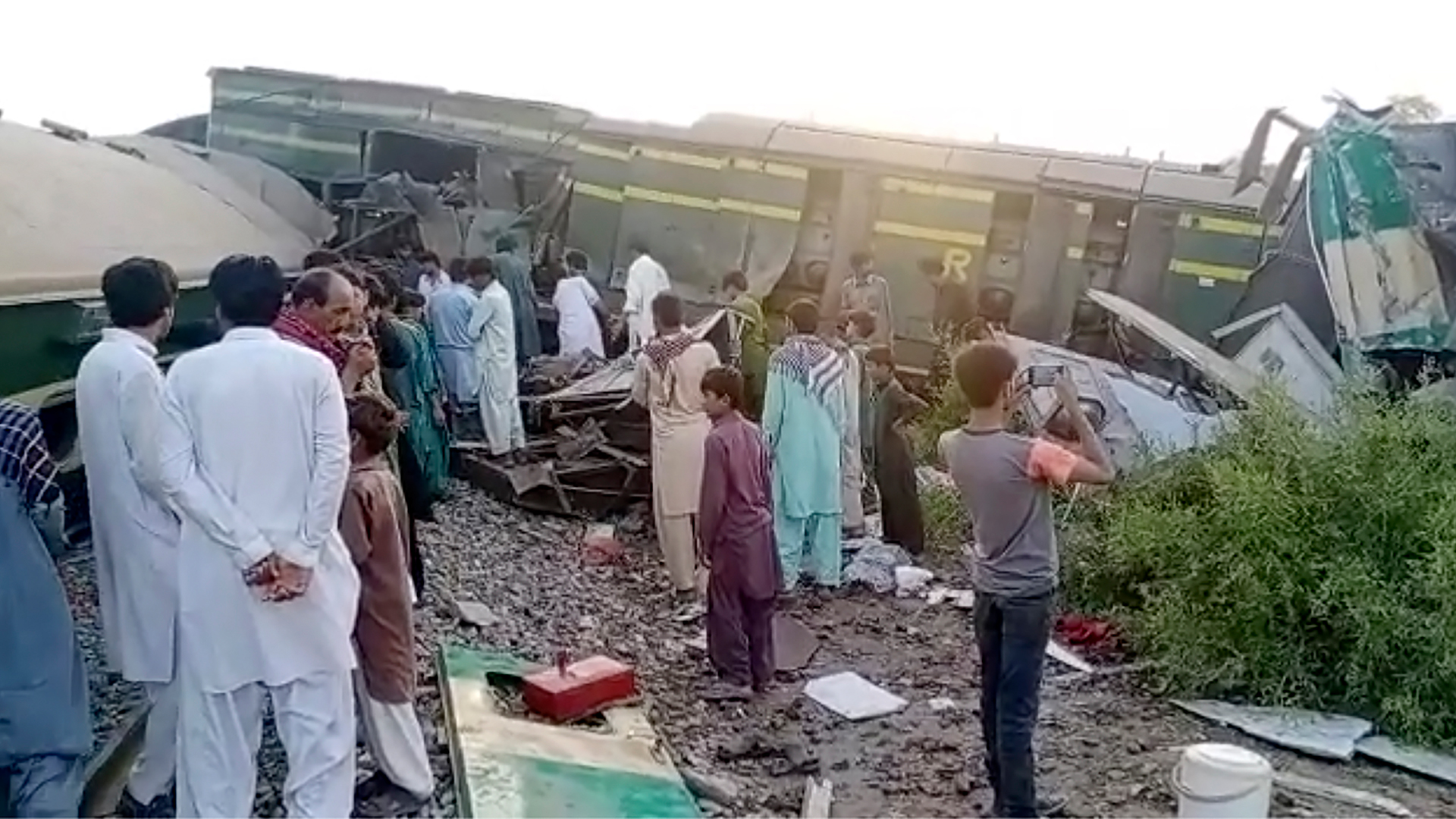 Menschen stehen neben Zügen, die in Ghotki (Pakistan) kollidiert sind. | dpa