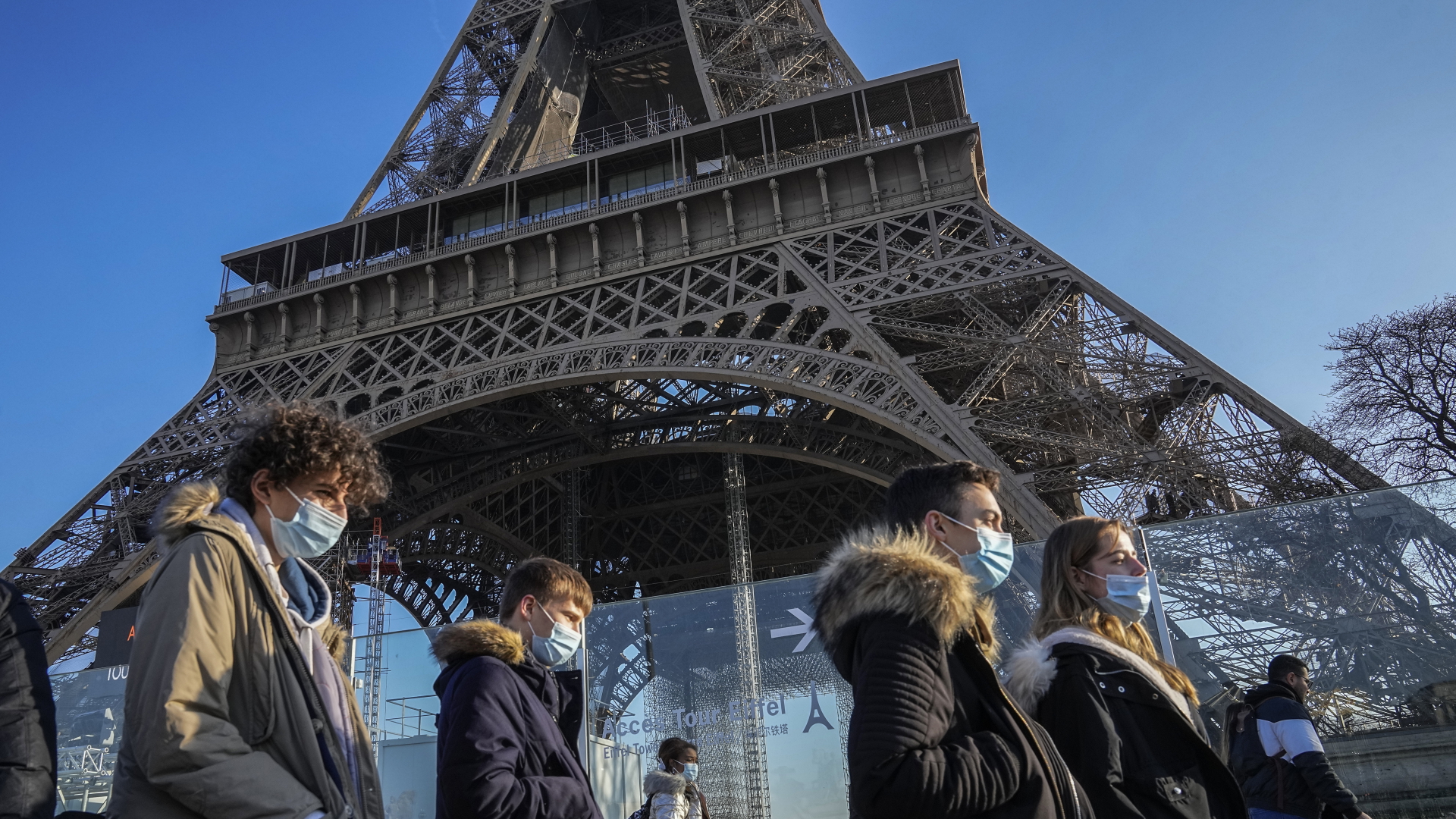 Menschen mit Schutzmasken gehen am Eiffelturm in Paris vorbei.