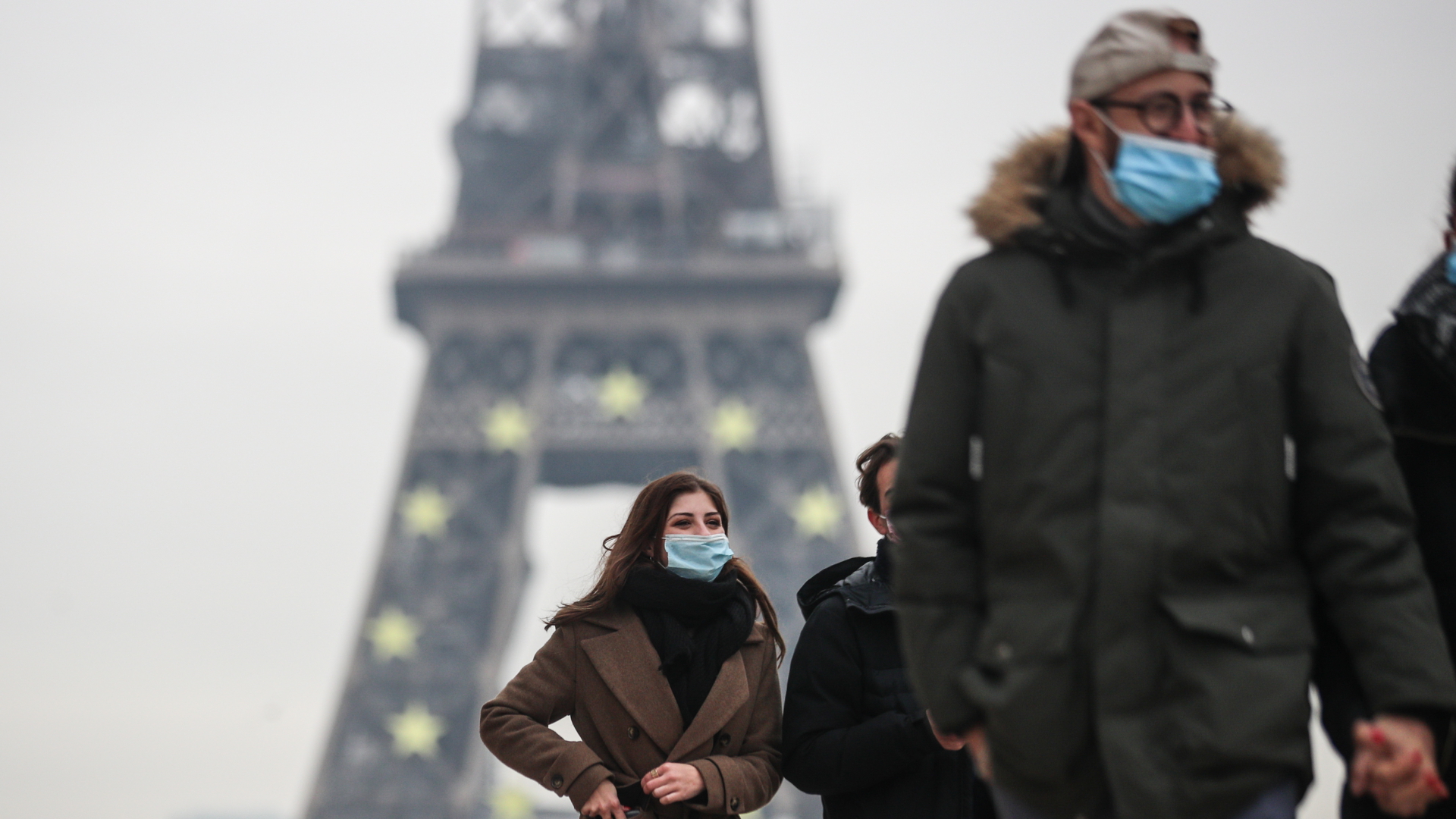 Menschen mit Makse gehen vor dem Eiffelturm in Paris entlang
