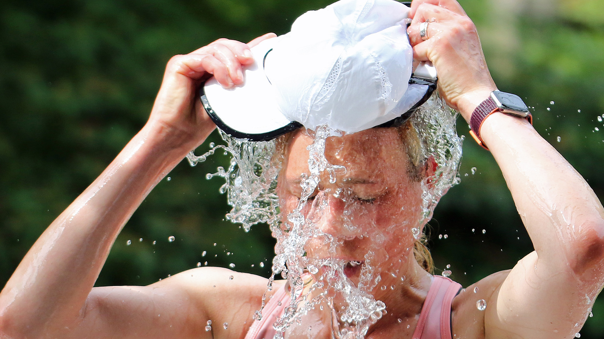 Eine Frau füllt an einer Erfrischungsstation ihre Mütze mit Wasser und kippt sich diese über den Kopf. | dpa