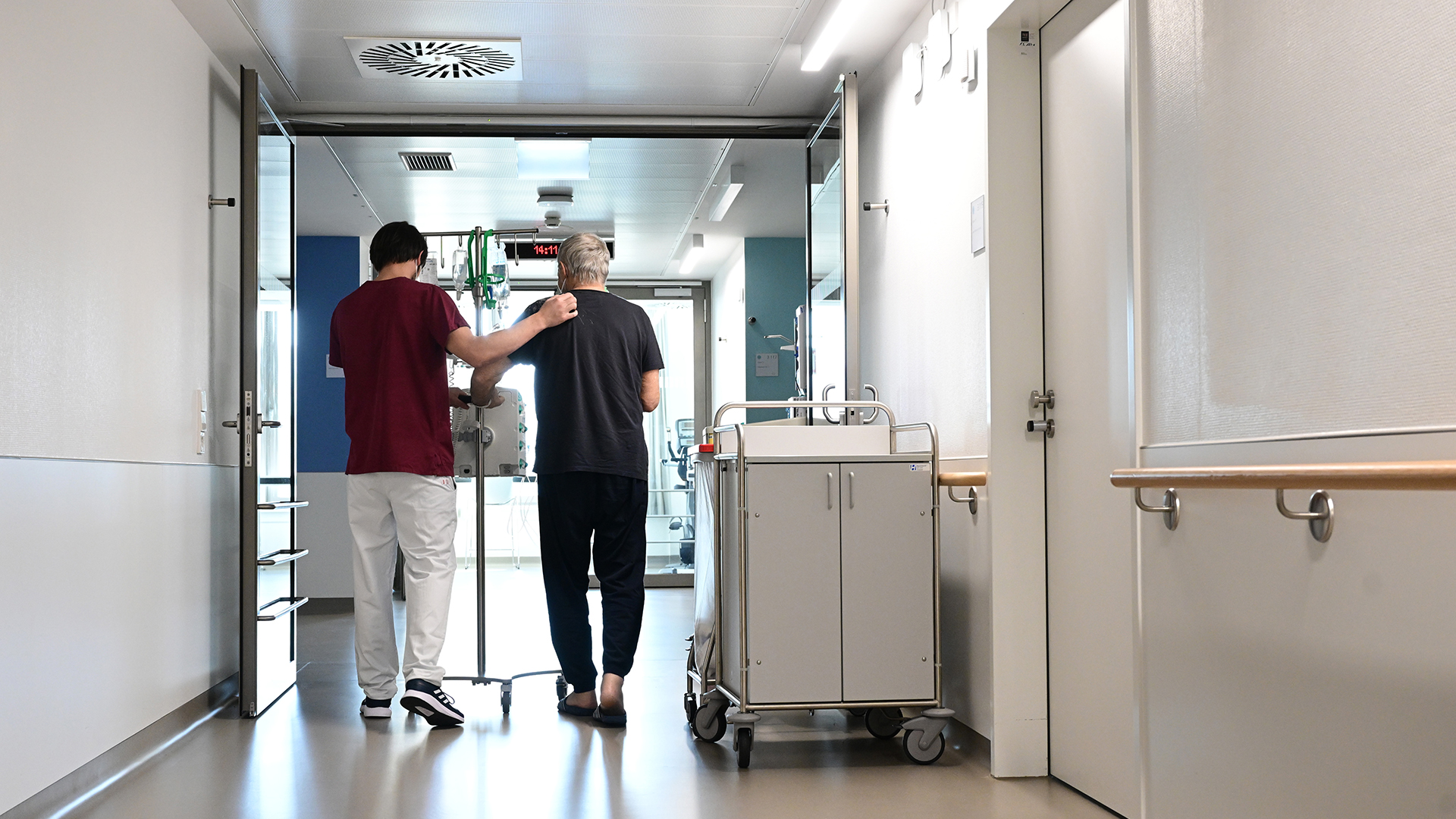 Ein Pfleger geht in einem Krankenhaus mit einem Patienten über einen Flur.