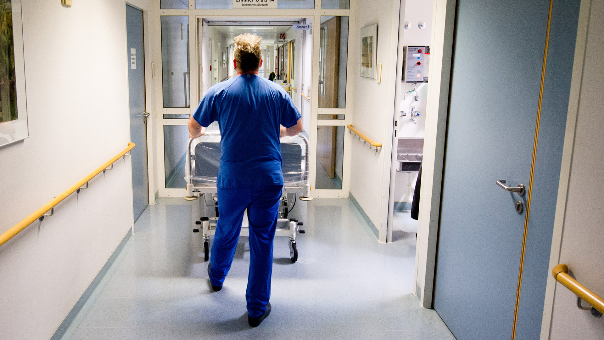 Ein Krankenpfleger schiebt  in einer Klinik in Berlin ein Krankenbett durch den Flur. | dpa
