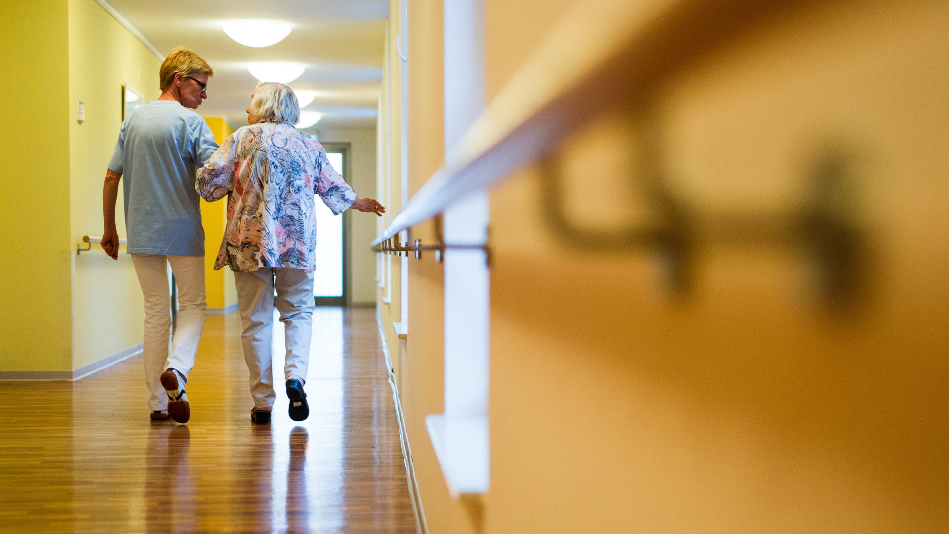 Eine Pflegekraft geht in einem Pflegeheim mit einer älteren Dame über einen Korridor.  | dpa