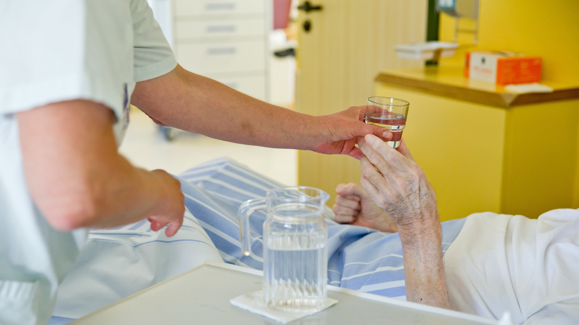 Eine Pflegerin reicht einer Patientin ein Glas Wasser. | dpa