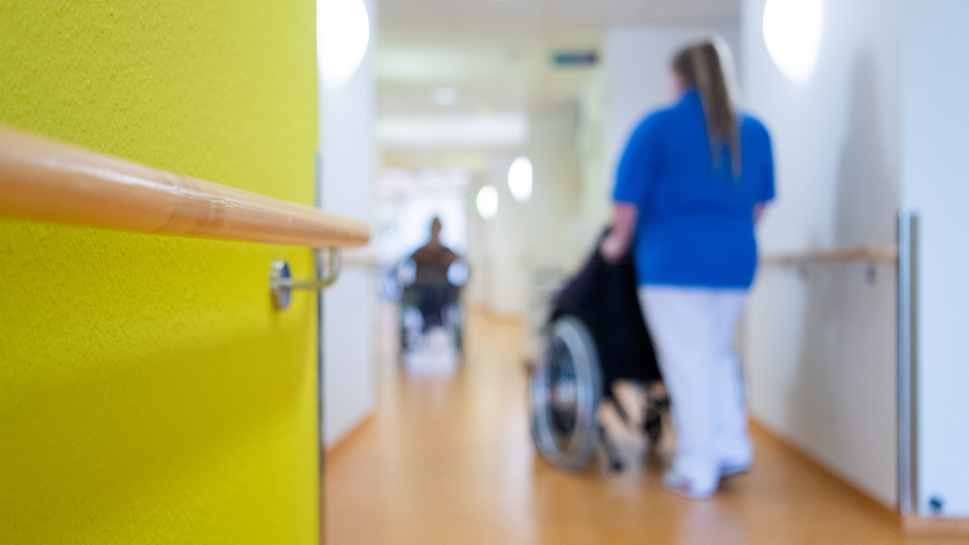 Pflegerin schiebt Patienten im Rollstuhl | dpa