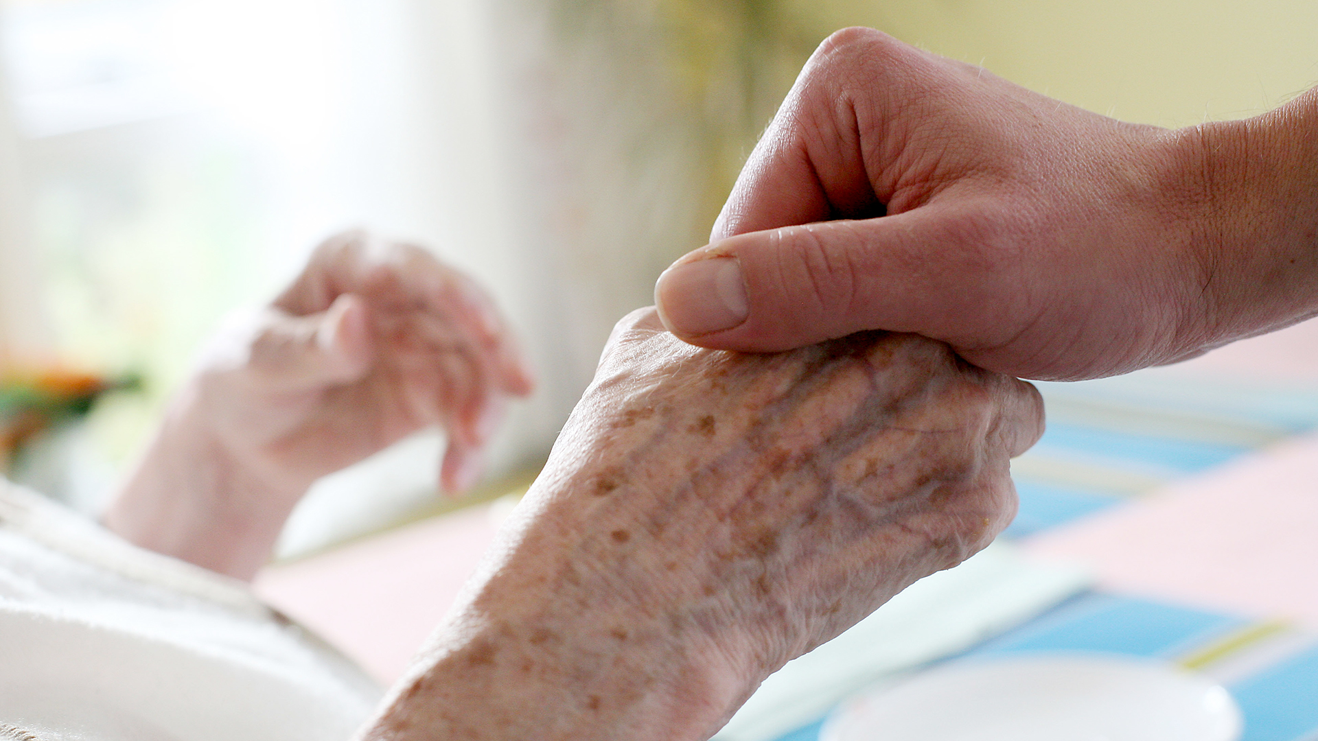 Ein Pfleger hält die Hand einer alten Frau.