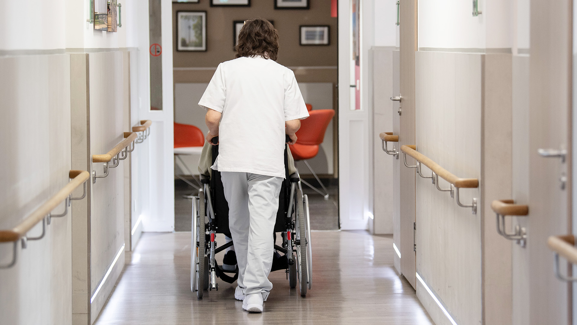 Eine Pflegerin schiebt einen Patienten im Rollstuhl. | dpa