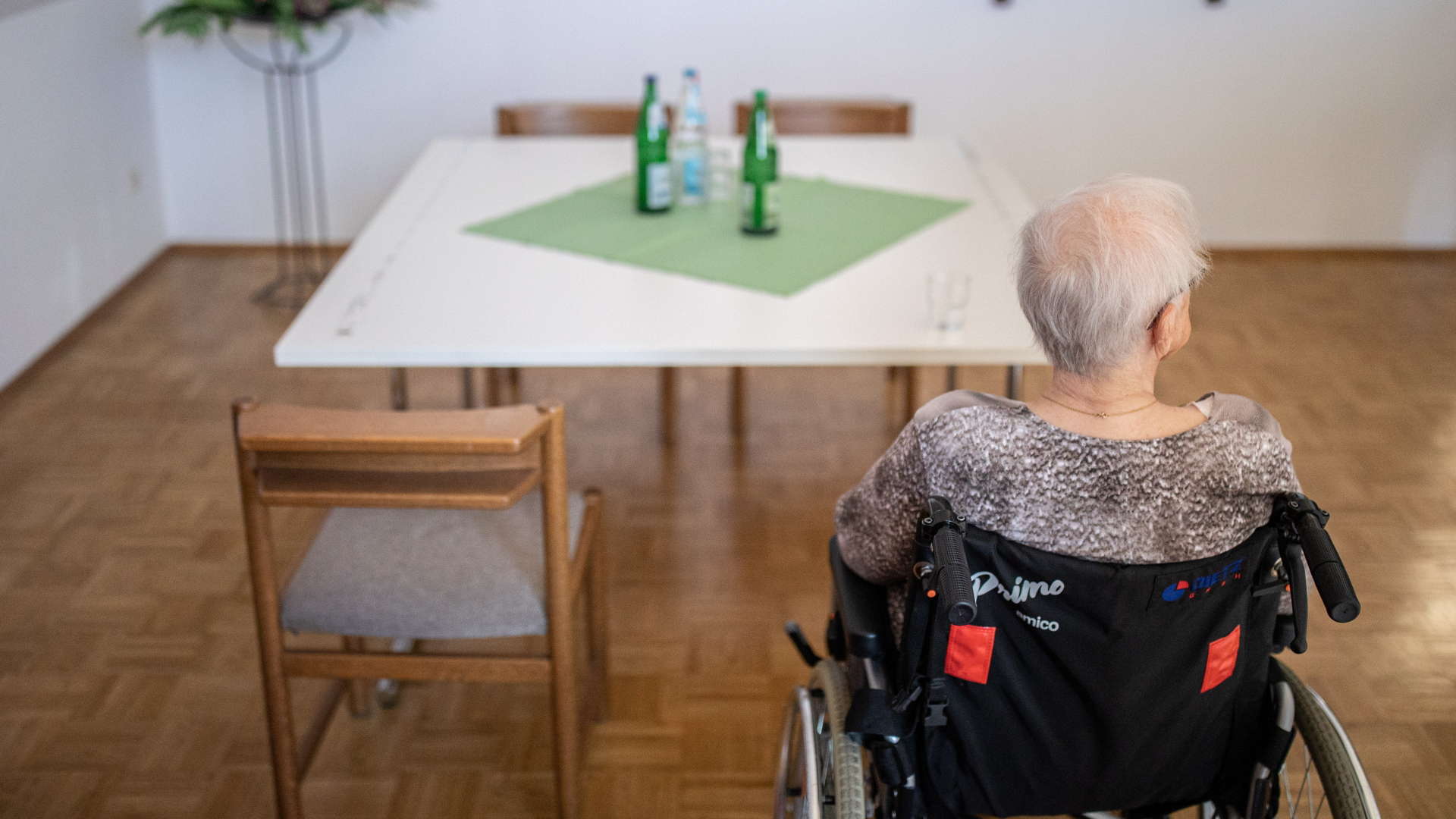 Eine ältere Frau sitzt in einem Pflegeheim in ihrem Rollstuhl vor einem Tisch.  | dpa
