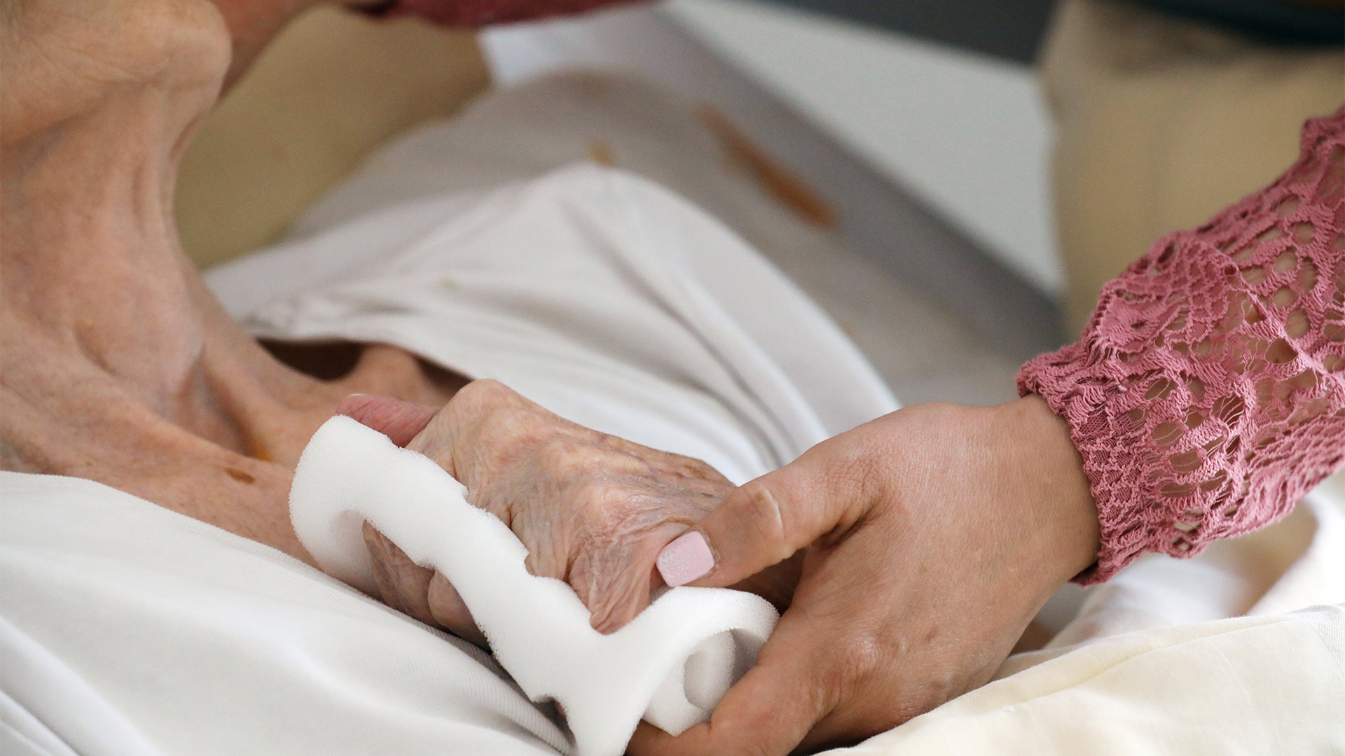 Eine Pflegeschwester hält die Hand einer alten Heimbewohnerin.