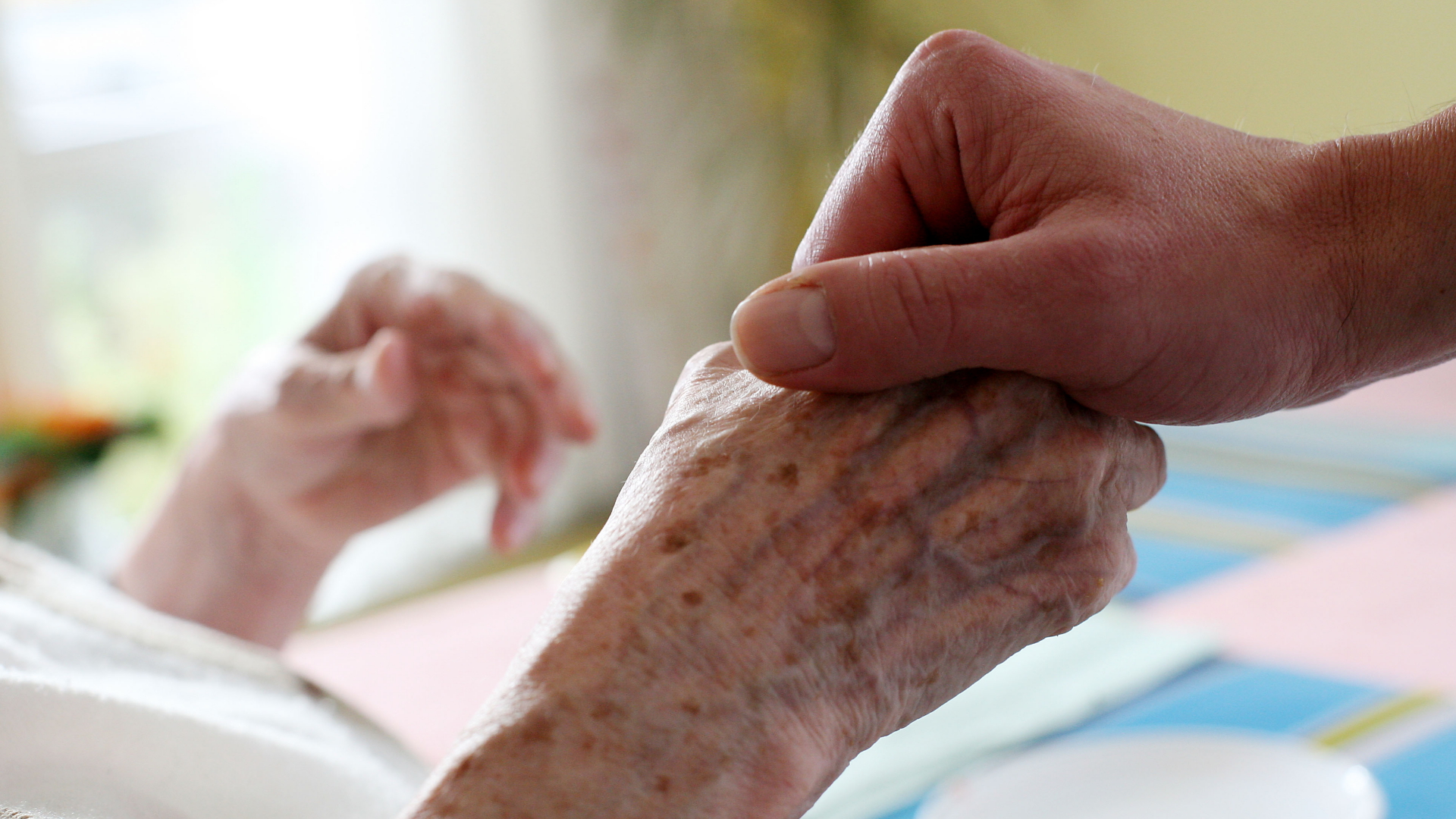 Eine Pflegekraft hält die Hand einer alten Person im Pflegeheim. | dpa