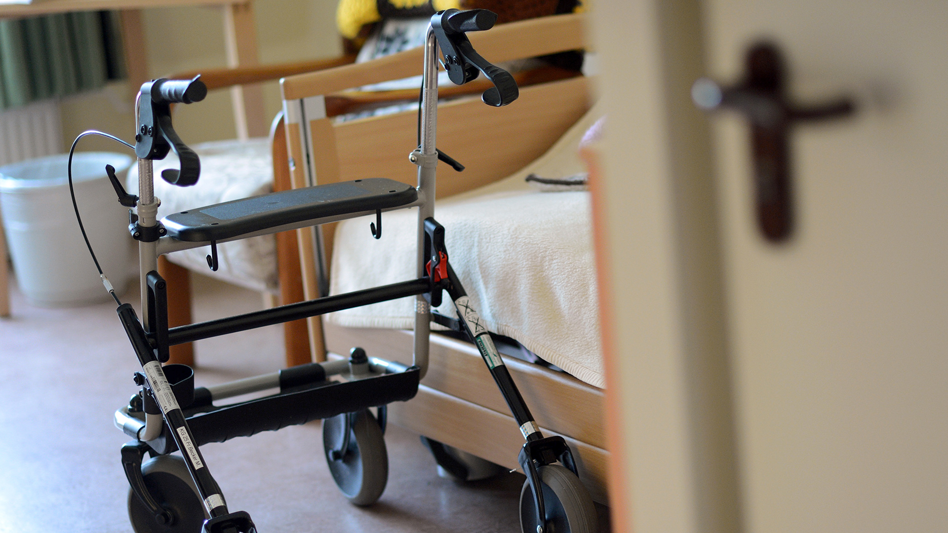 Ein Rollator steht in einem Seniorenheim in einem Zimmer neben einem Pflegebett.