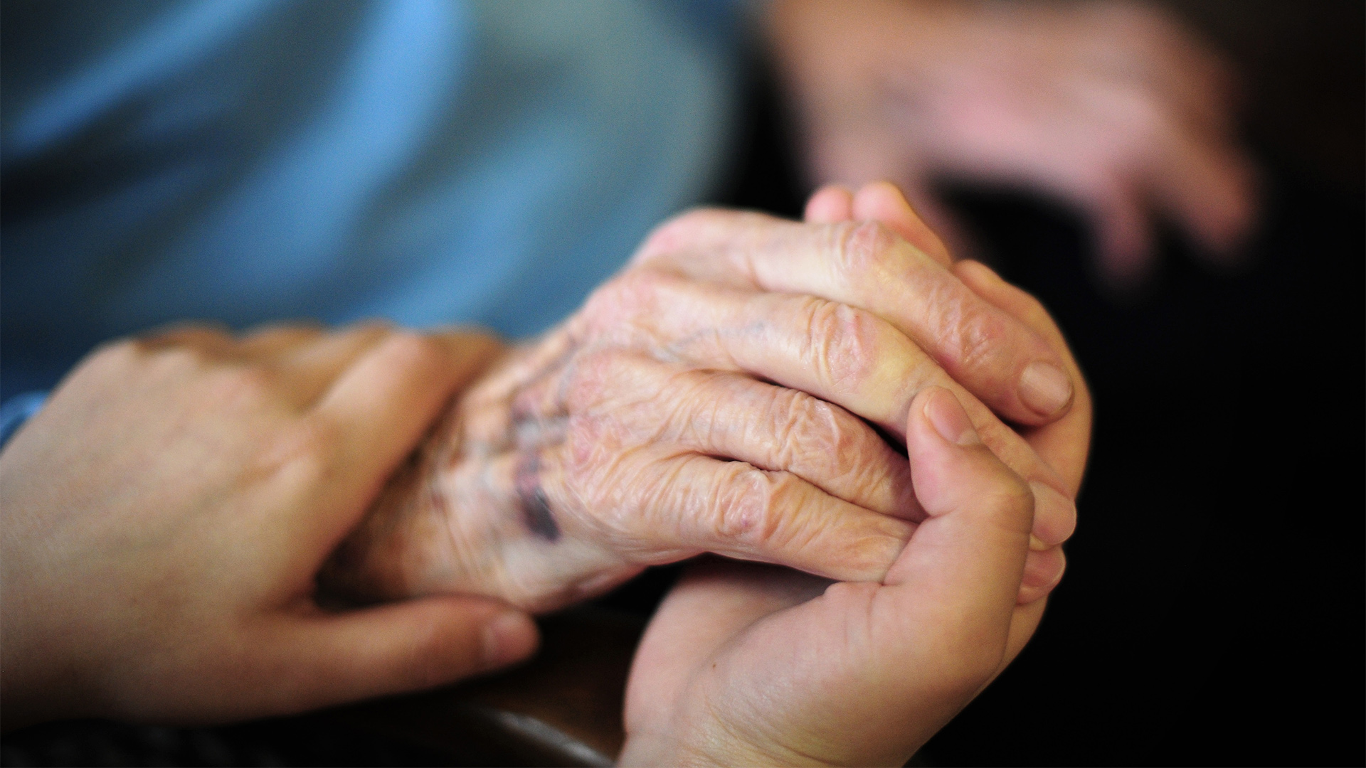 Eine Pflegekraft hält die Hand einer alten Frau.