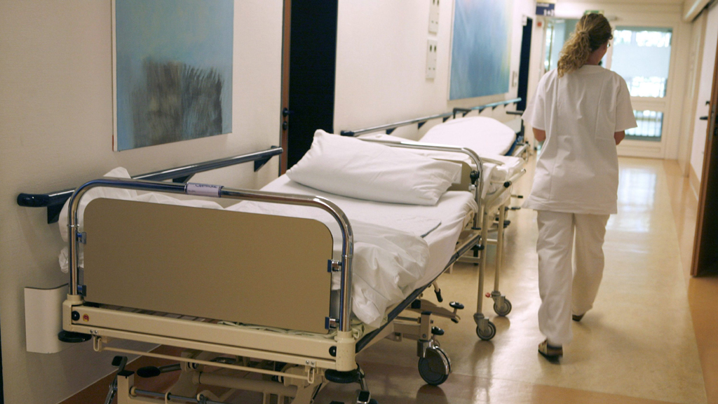 Ein Krankenschwester eilt auf einem Flur an einem leeren Bett vorbei | dpa