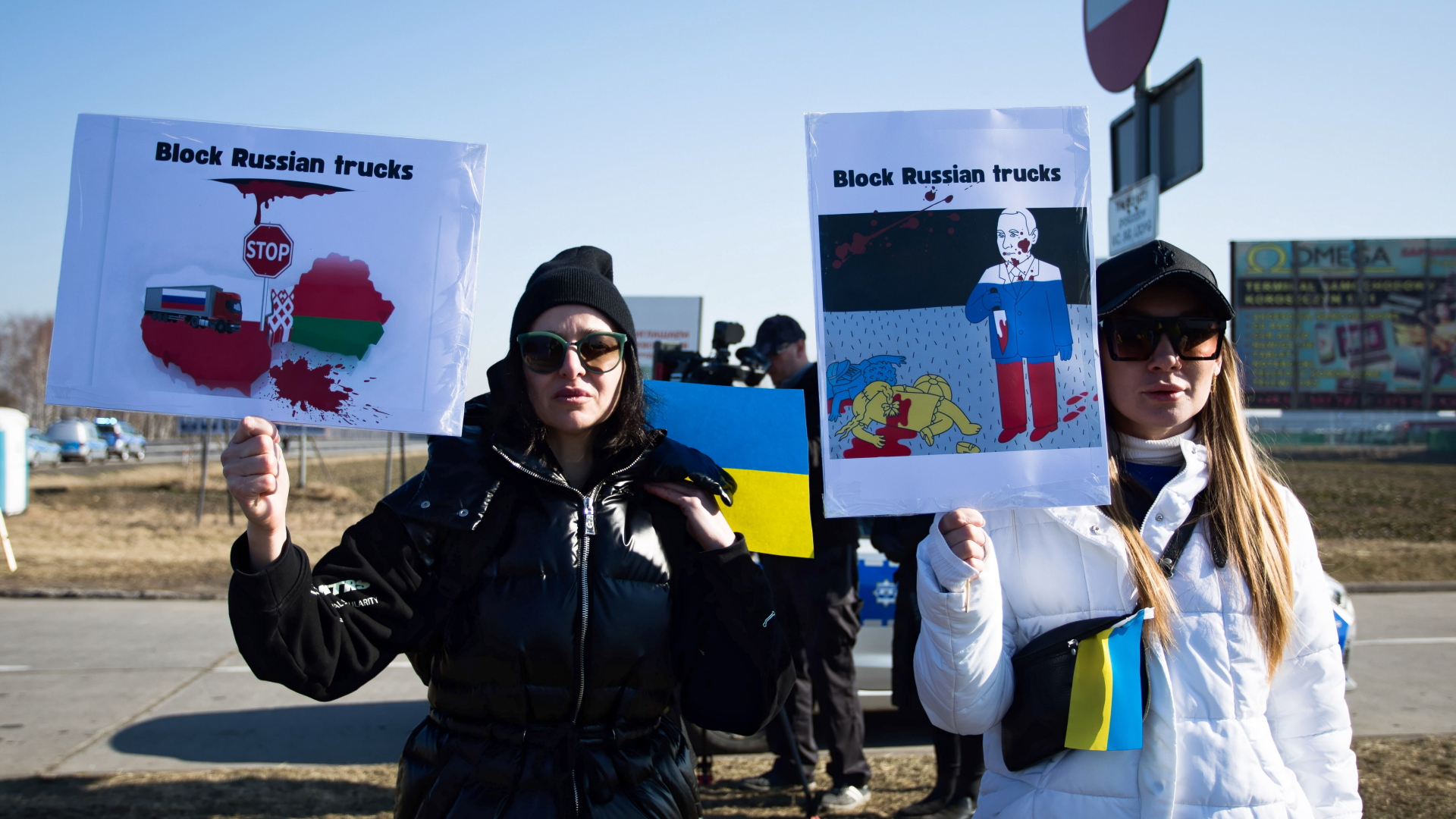 "Block Russian trucks" steht auf Protestschildern, die zwei Demonstrantinnen an der polnisch-belarusischen Grenze hochhalten. | EPA