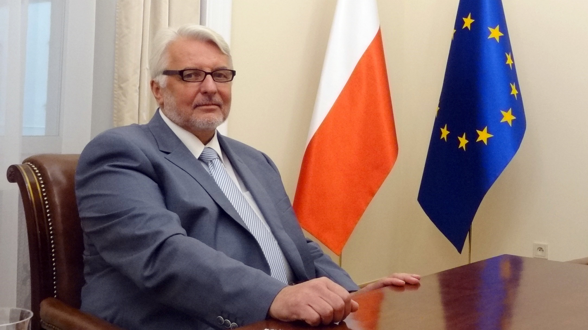 Polens Außenminister Waszczykowski sitzt am Schreibtisch, im Hintergrund die Flaggen von Polen und der EU. | dpa