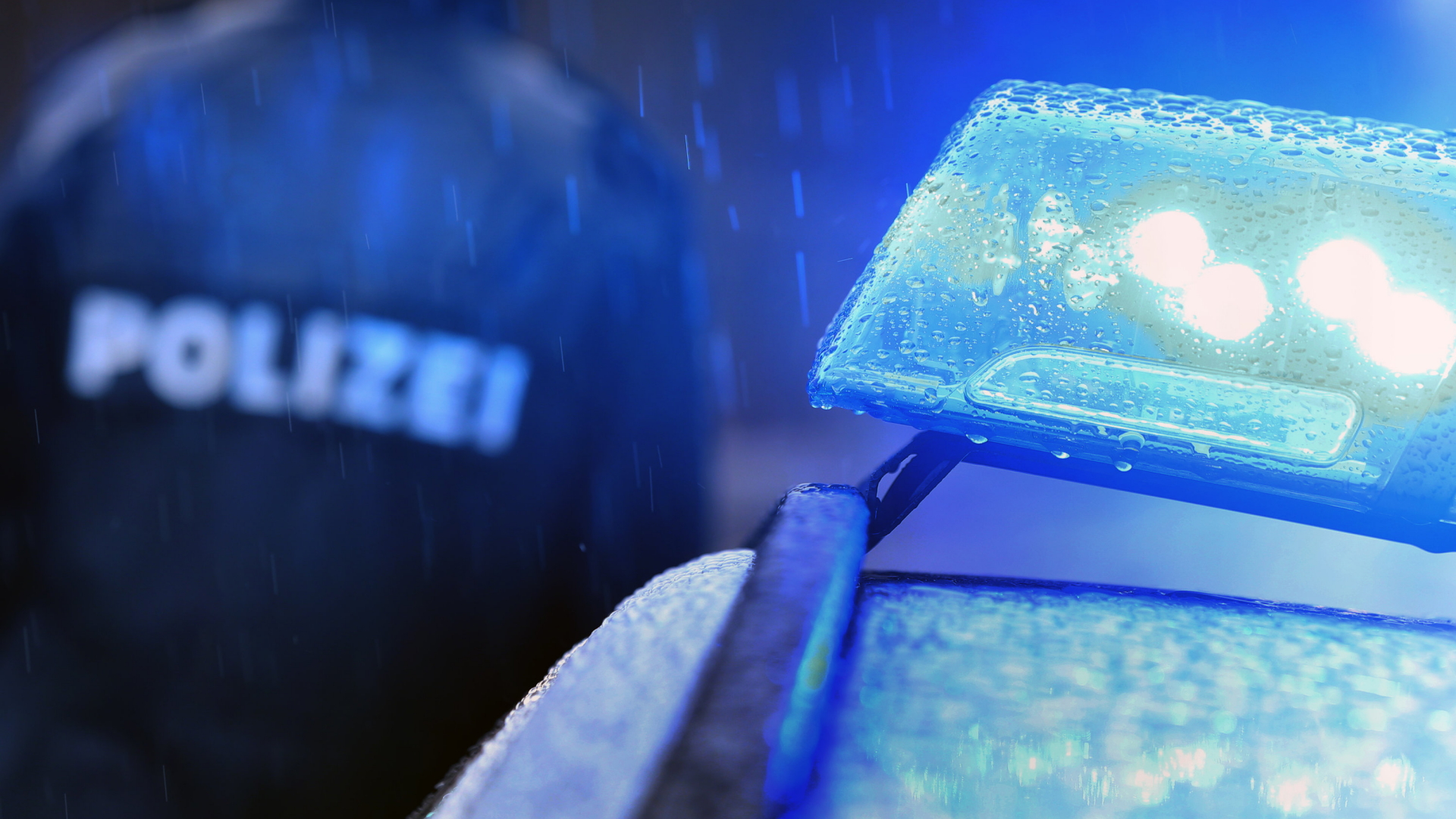 Polizist neben einem Streifenwagen mit Blaulicht (Symbolbild) | dpa
