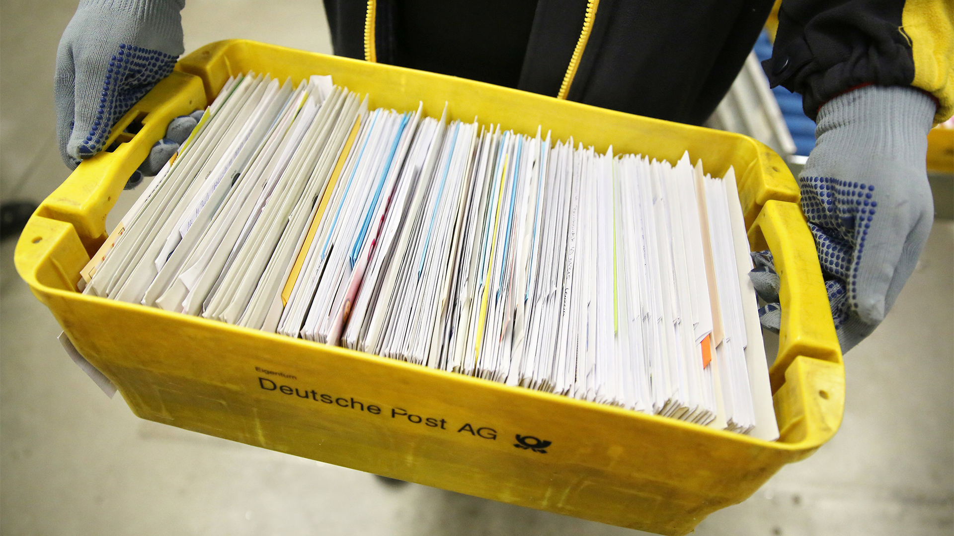 Eine Mitarbeiterin der Deutschen Post trägt eine Kiste mit Briefen