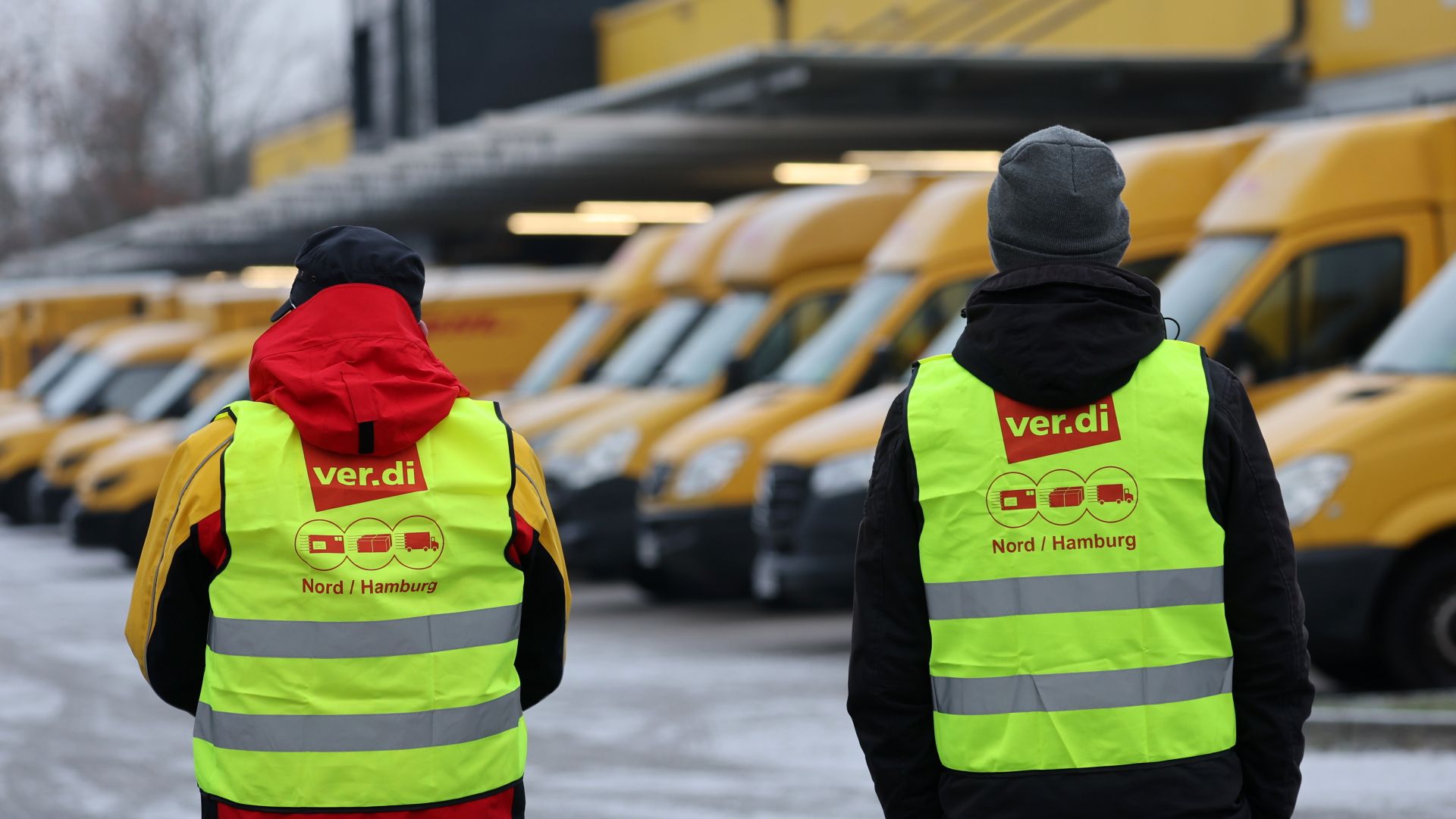 DHL-Mitarbeiter stehen vor Lastwagen und streiken. | dpa