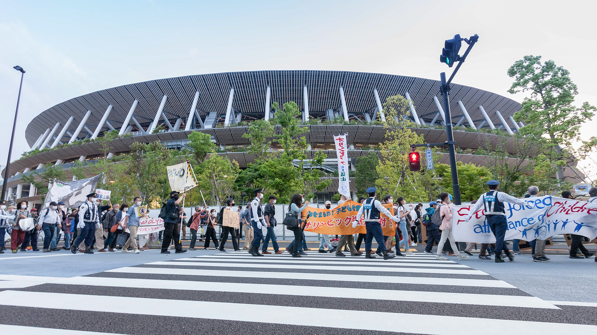 Demonstranten halten vor dem Nationalstadion in Tokio (Japan) Schilder gegen die Austragung der Olympischen Spiele in die Höhe. | dpa