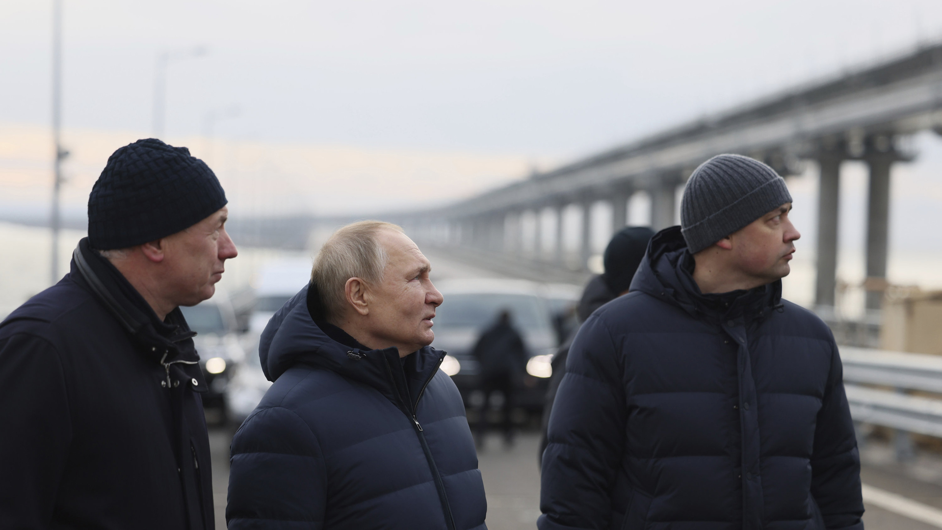 Wladimir Putin (mitte), Marat Chusnullin (links) un d eine weitere Person gucken auf eine Brücke. | AP
