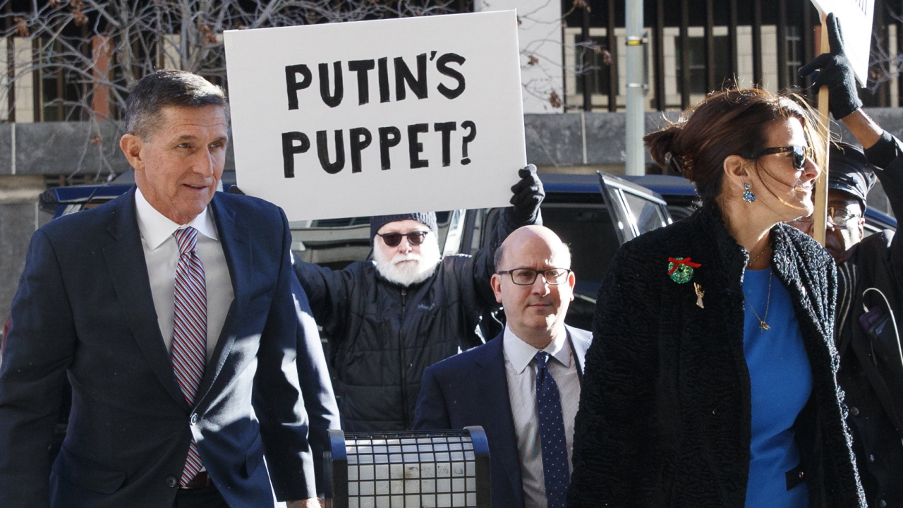 Während Trumps Ex-Bearter Flynn vor Gericht erscheint, hält hinter ihm ein Mann ein Schild mit den Worten "Putin's Puppet?" | dpa