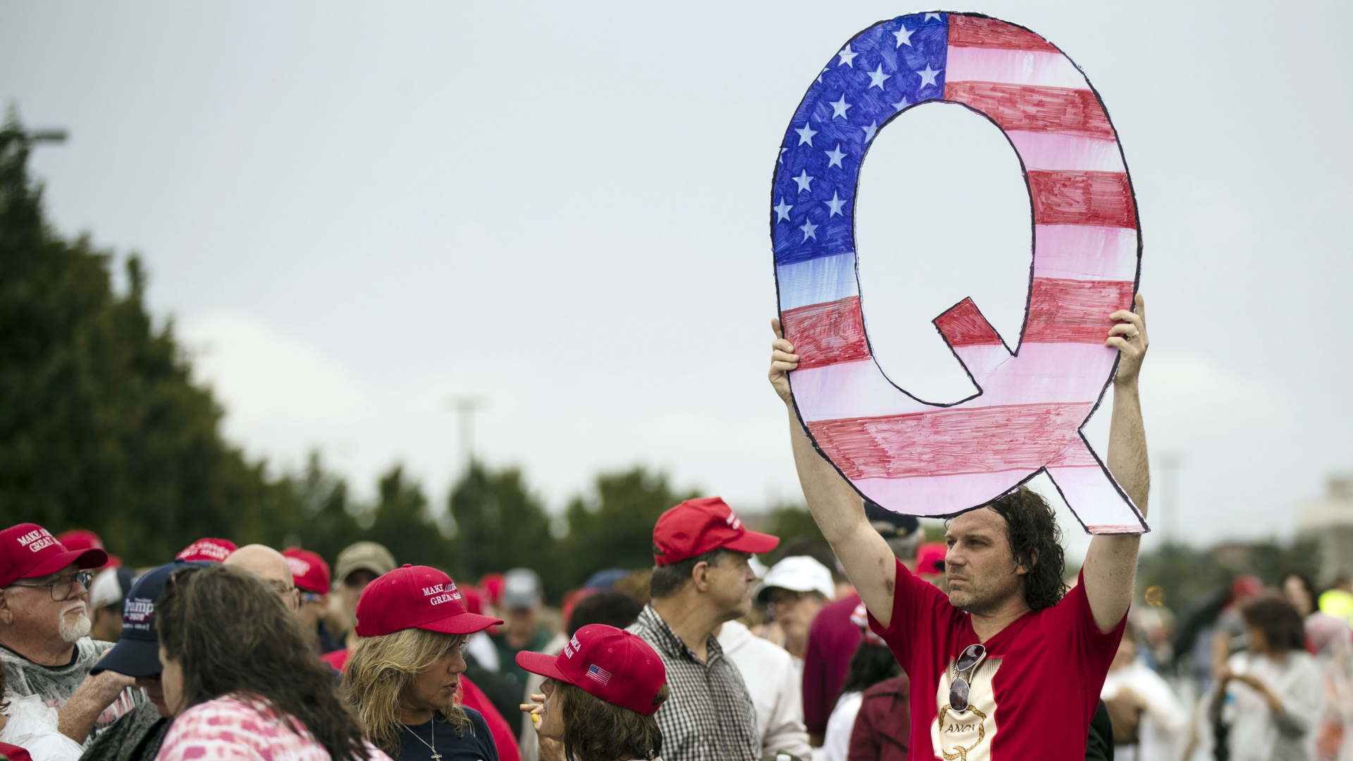 Ein Anhänger der QAnon-Bewegung hält einen großen Pappbuchstaben in die Luft. | AP