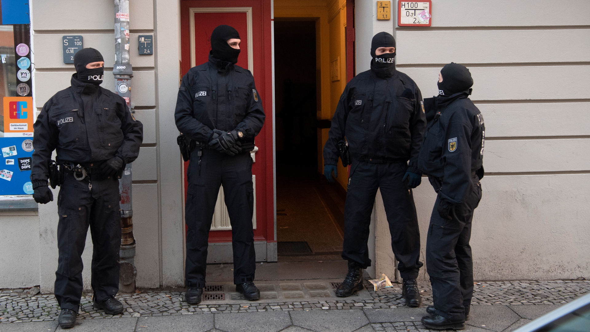 Polizisten stehen bei einer Razzia gegen eine mutmaßliche Schleuserbande an einer Eingangstür von einem Gebäude in Berlin