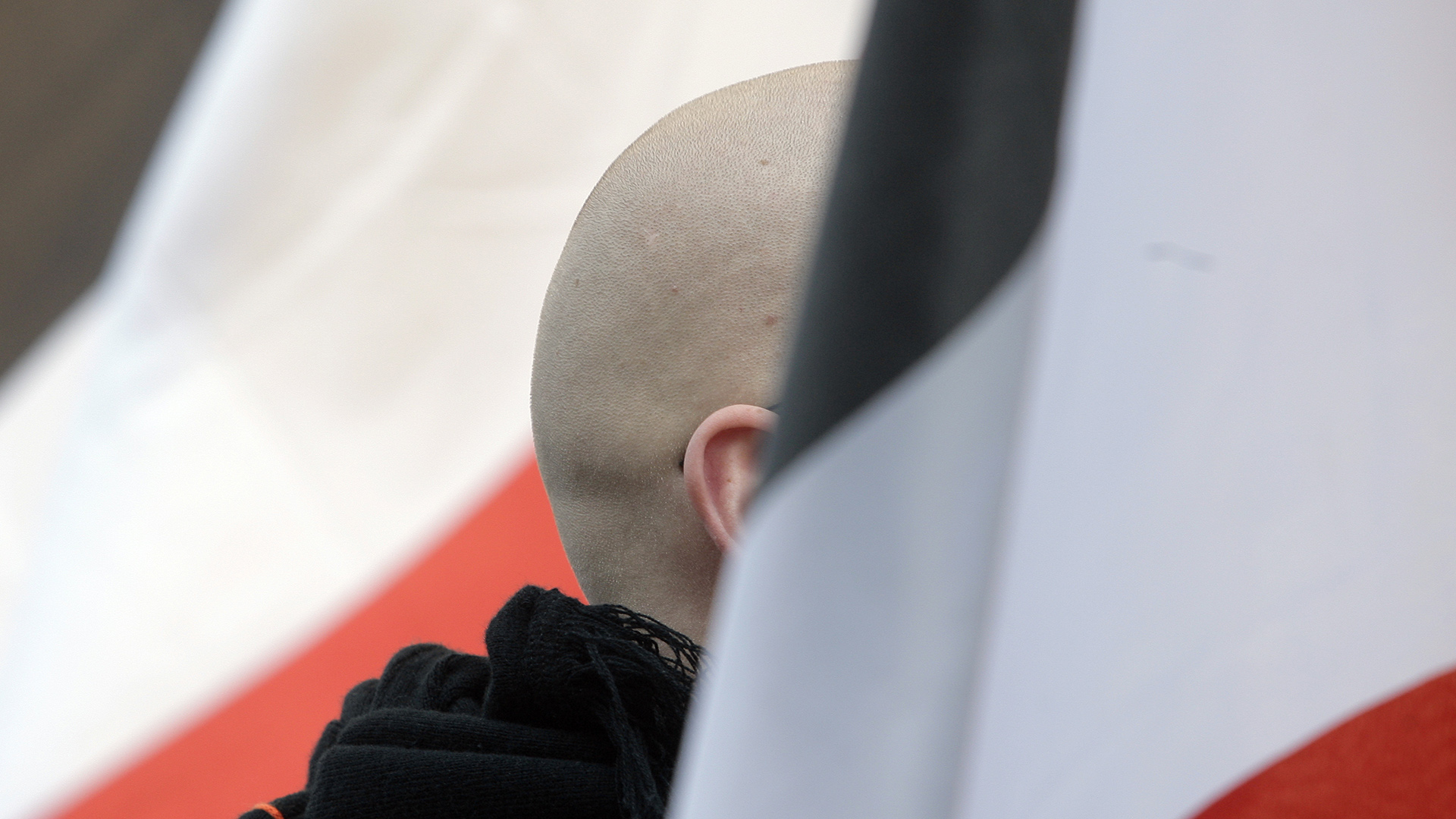 Ein Mann mit geschorenem Kopf steht zwischen schwarz-weiß-roten Fahnen während einer Demonstration von Rechtsextremen. | dpa