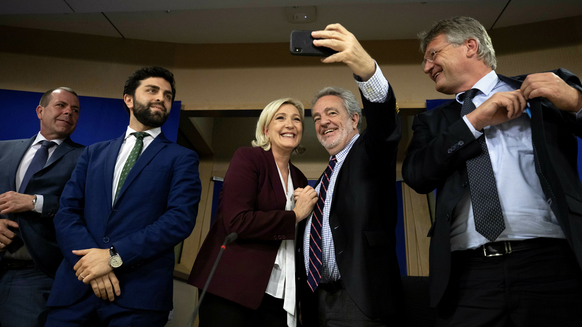 RN-Chefin Le Pen und Vlaams Belang-Politiker Gerolf Annemans nehmen am Rande der Pressekonferenz eine Selfie auf. Rechts von ihnen steht AfD-Chef Meuthen. | AP