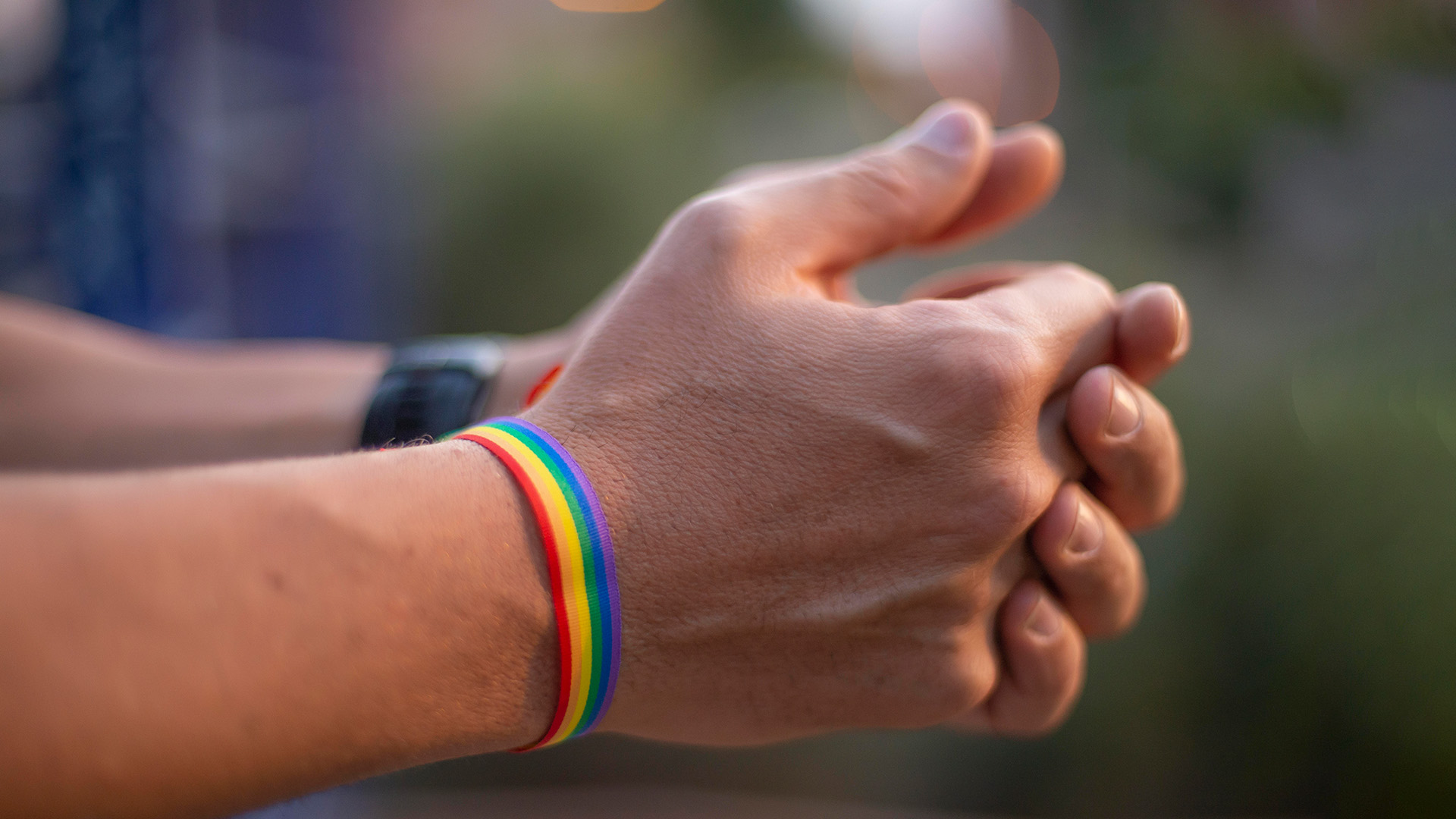 Hände eines Mannes mit einem Armband in Regenbogenfarben (Symbolbild).