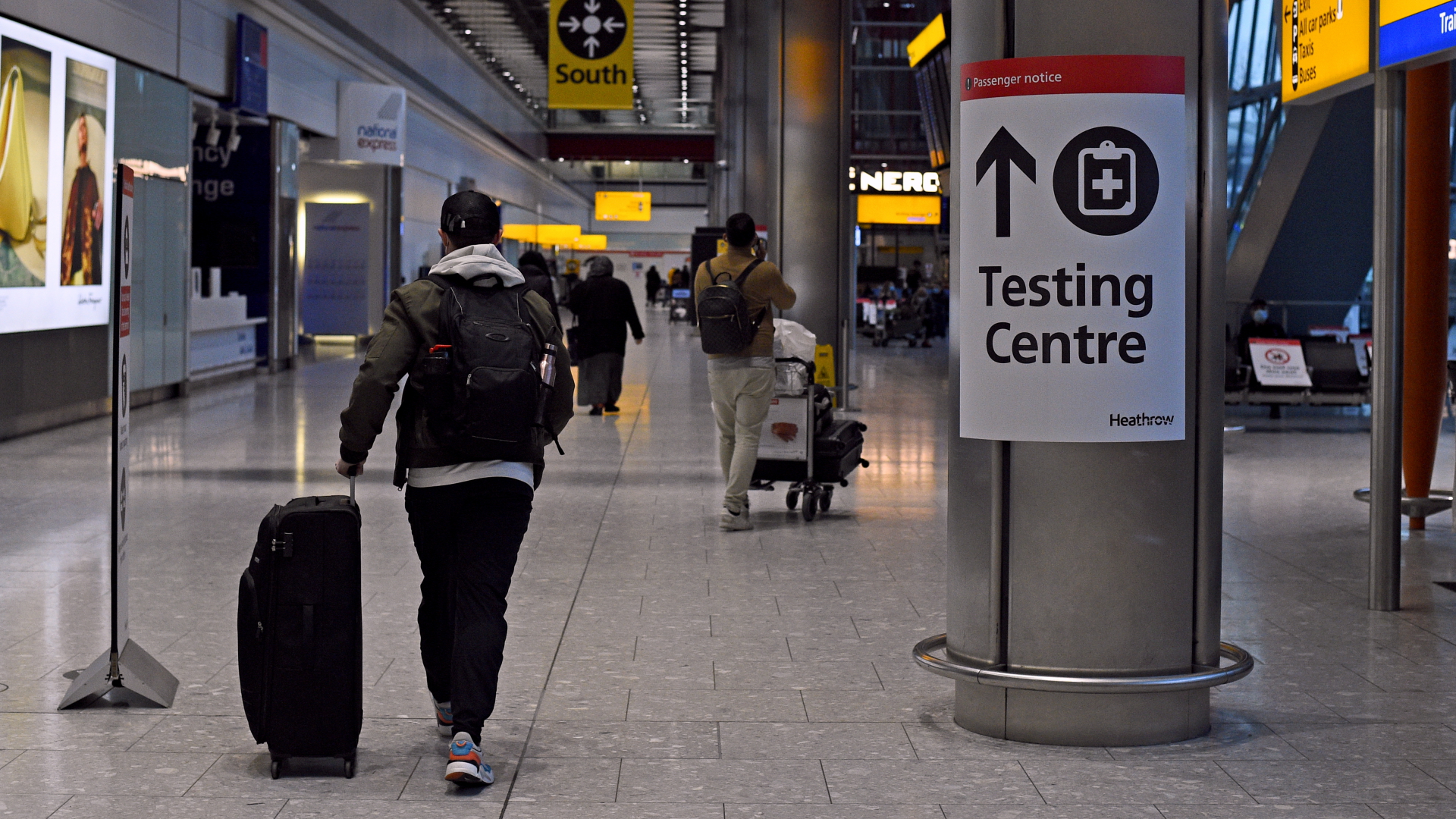 Ein Passagier geht nach seiner Ankunft in England an einem Schild in der Ankunftshalle von Terminal 5 am Londoner Flughafen Heathrow vorbei, das den Weg zu einem Corona-Testzentrum anzeigt. | dpa