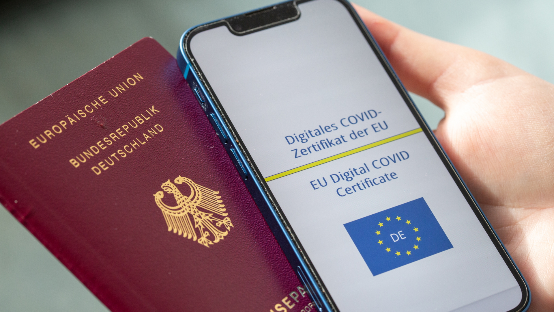 Eine Person hält ein Smartphone, das das digitale Covid-Zertifikat der EU zeigt, und einen deutschen Reisepass. | dpa
