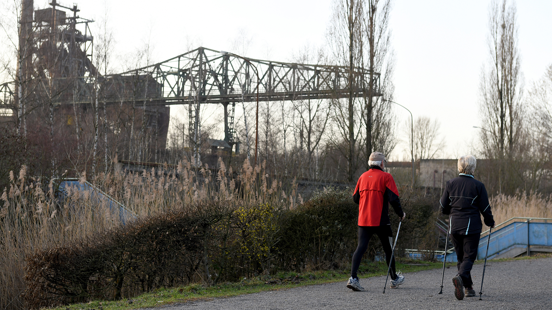Ein Ehepaar walkt am frühen Morgen an den alten Hochöfen im Landschaftspark Duisburg Nord vorbei.