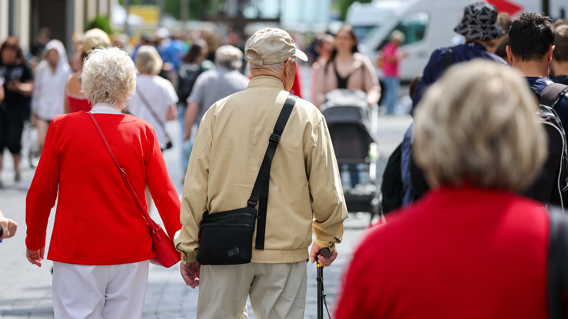 Ein älteres Paar geht zum Einkaufen durch eine Innenstadt. 