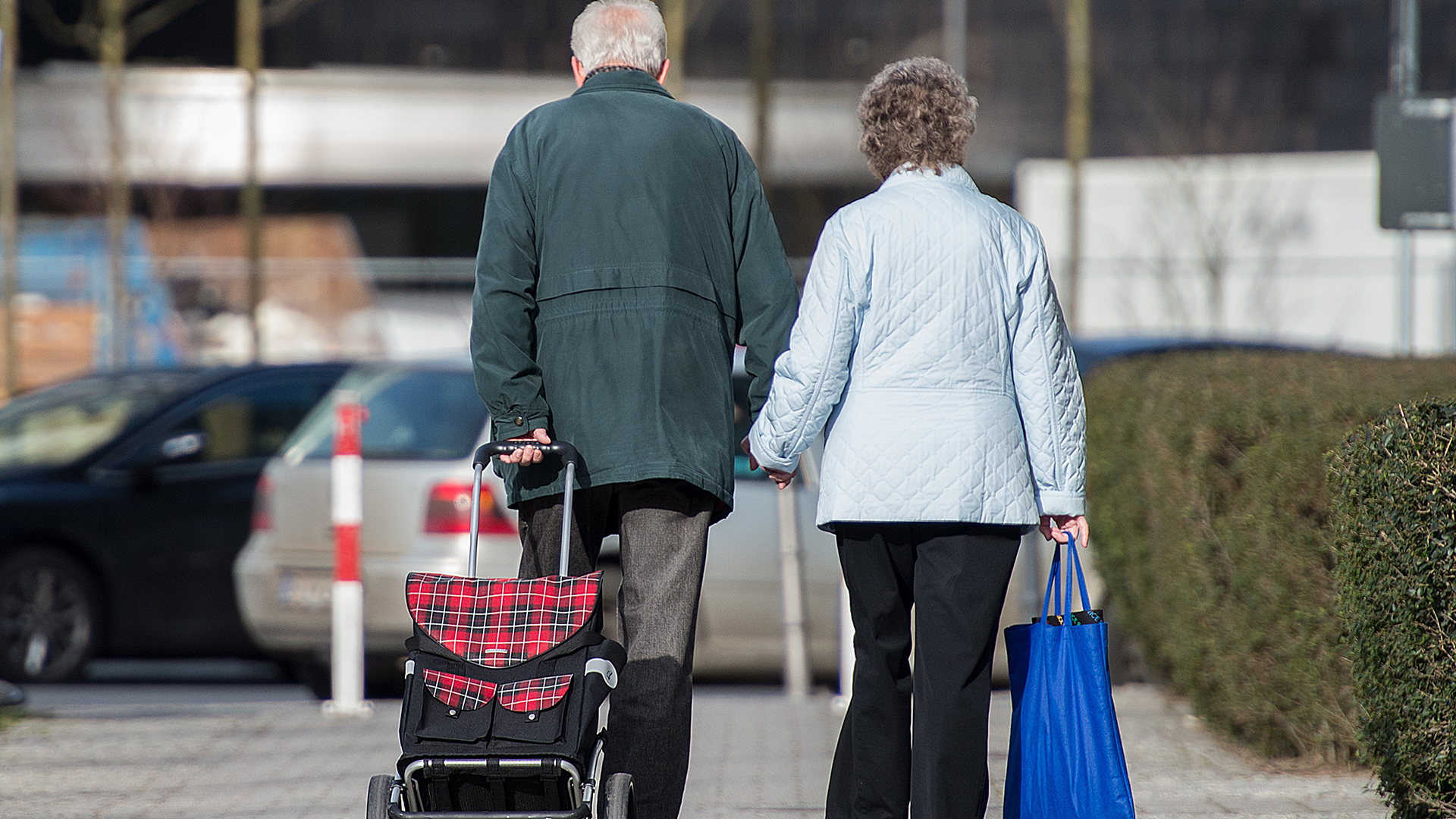 Ein älteres Paar mit Taschen geht händehaltend nebeneinander | dpa