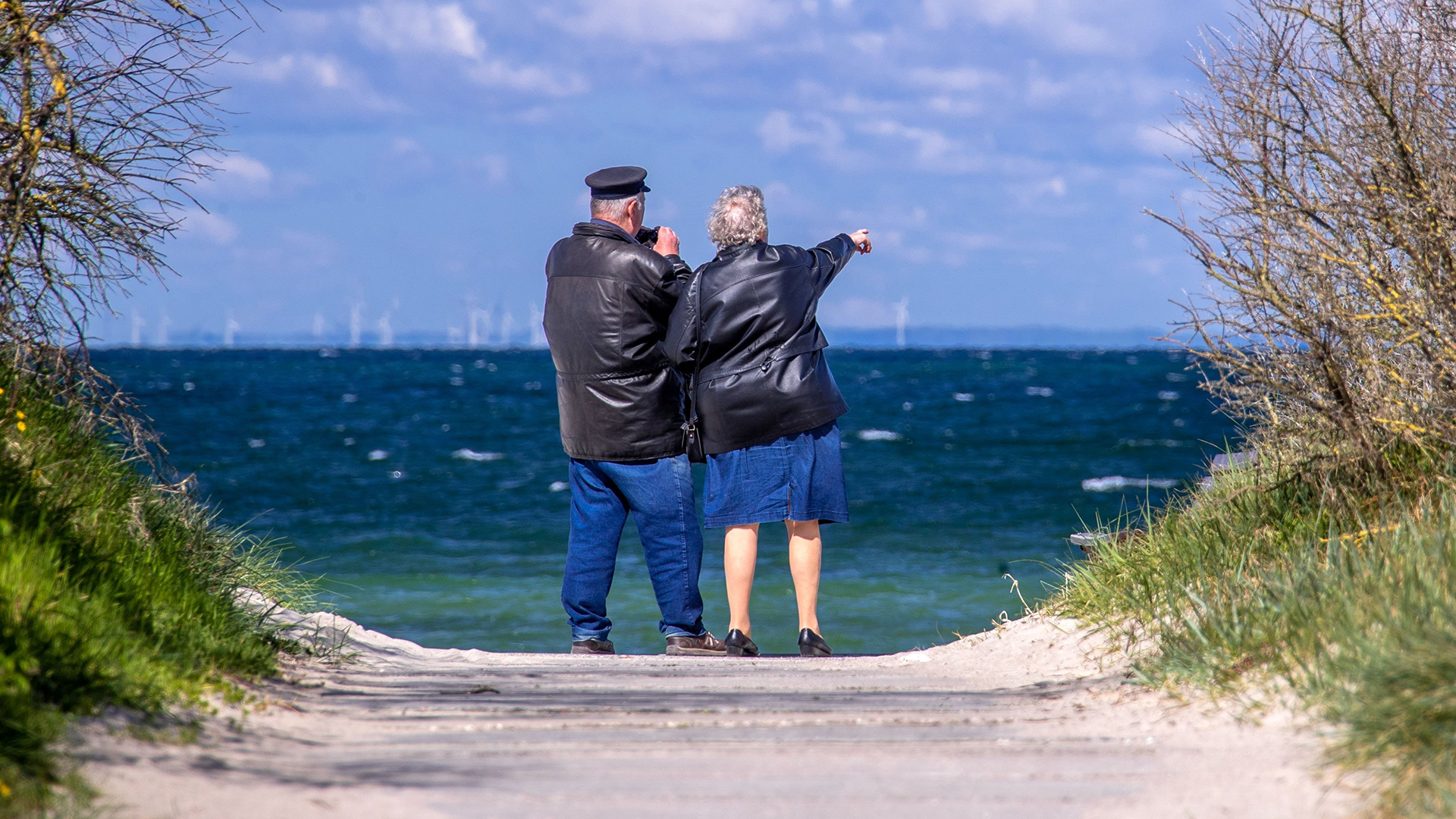 Ein Rentnerpaar steht am ansonsten menschenleeren Strand und schaut aufs Meer.
