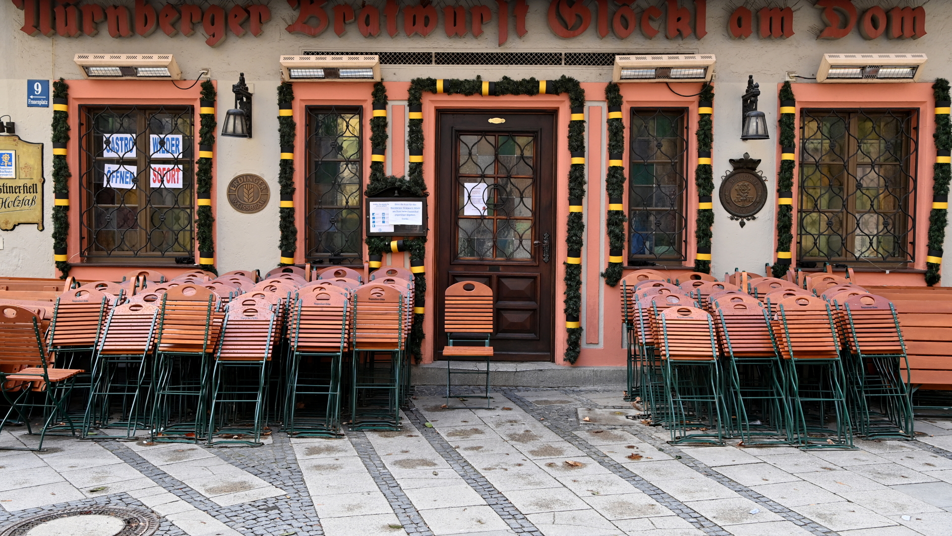 Zusammengestellte Stühle stehen vor einer geschlossenen Gaststätte in München. | dpa