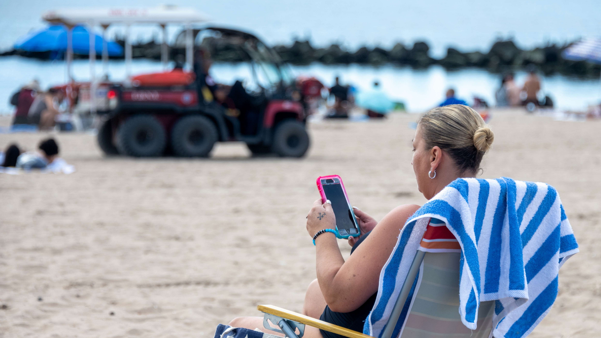Frau sitzt in einem Stuhl am Strand und schaut auf ihr Smartphone | AFP