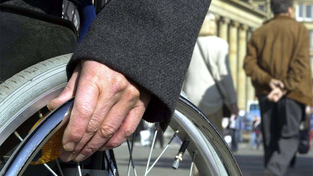 Die Hand eines Rollstuhlfahrers liegt auf dem Rad. | picture-alliance / dpa/dpaweb