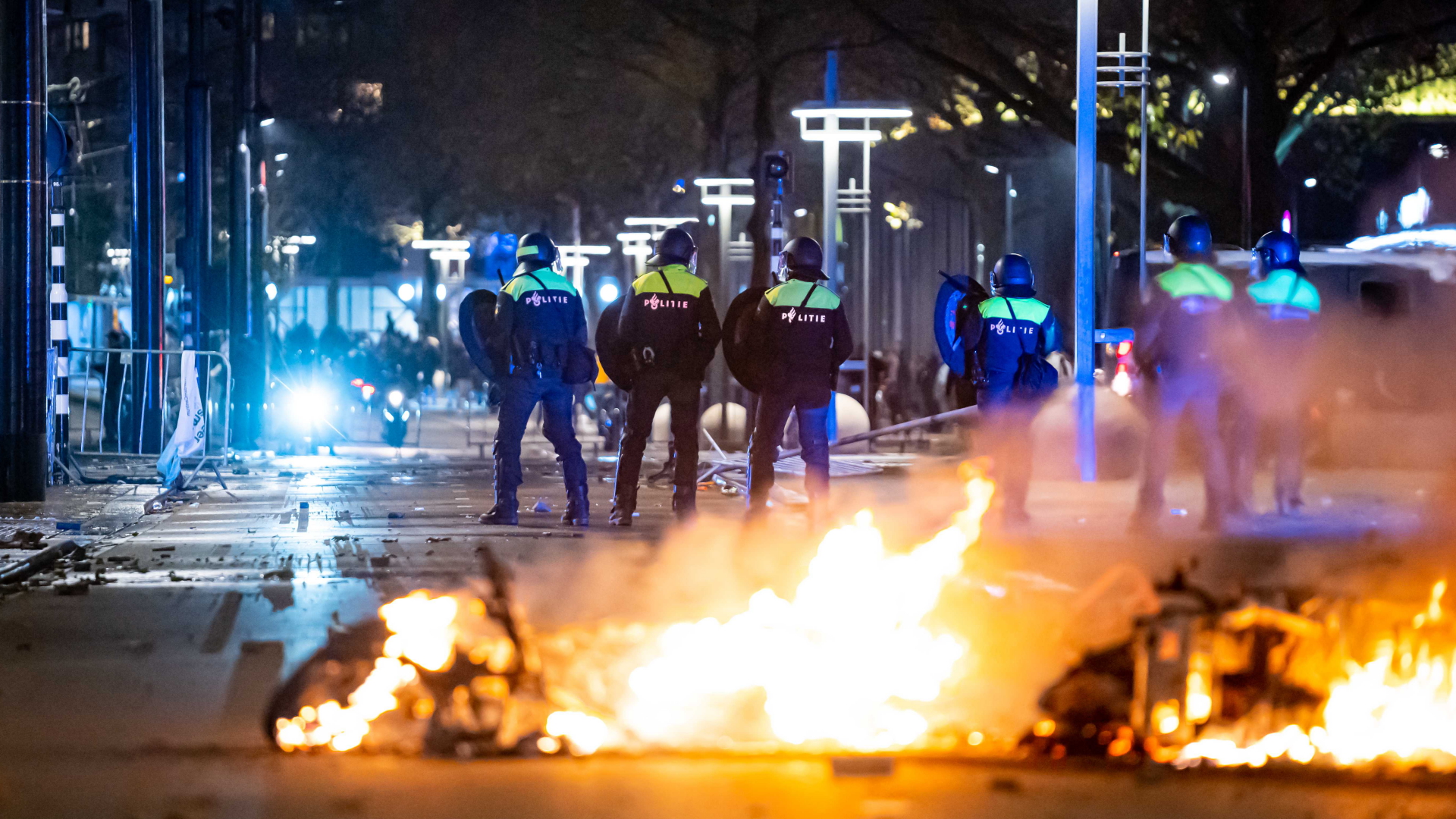 Polizisten stehen während der Ausschreitungen in Rotterdam vor einem Feuer auf der Straße. | dpa