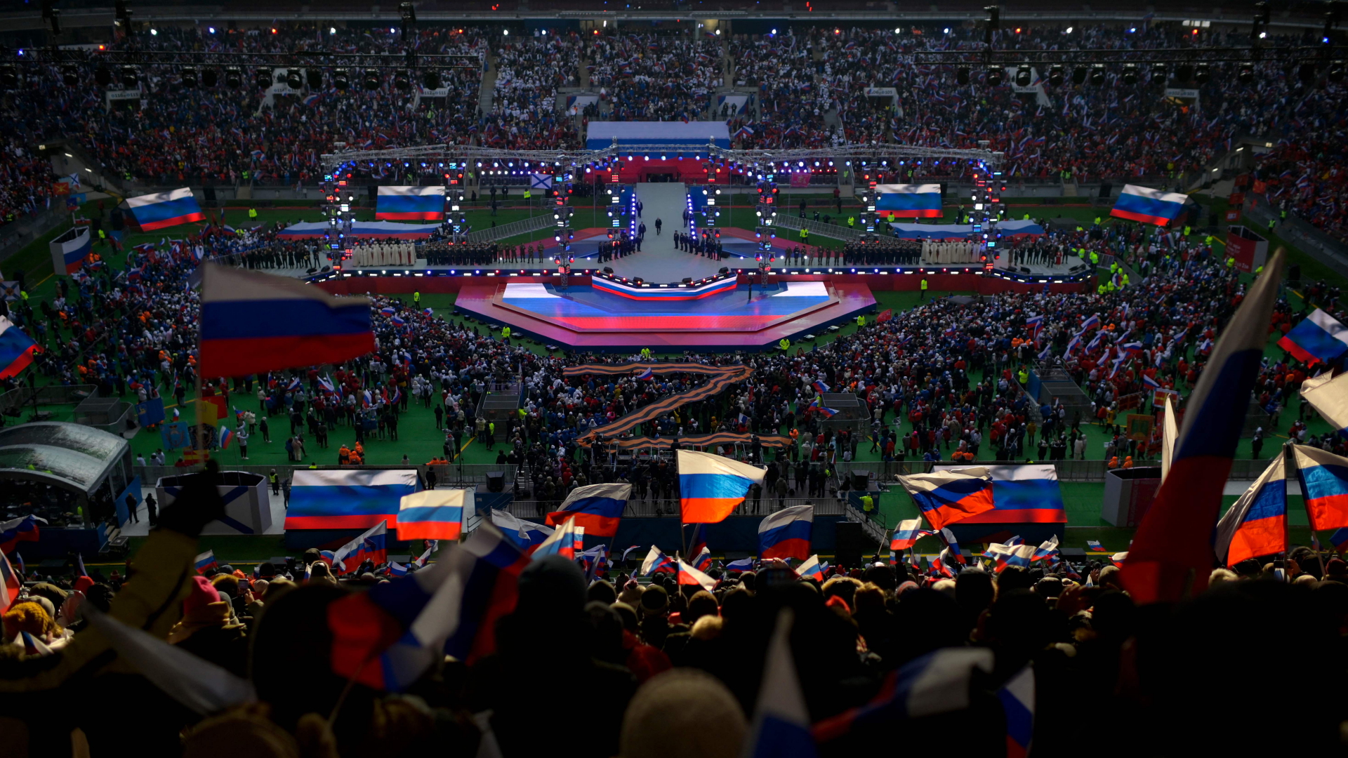 Menschen schwenken russische Fahnen, als Wladimir Putin die Bühne betritt, um eine Rede während eines patriotischen Konzerts zu halten. | AFP