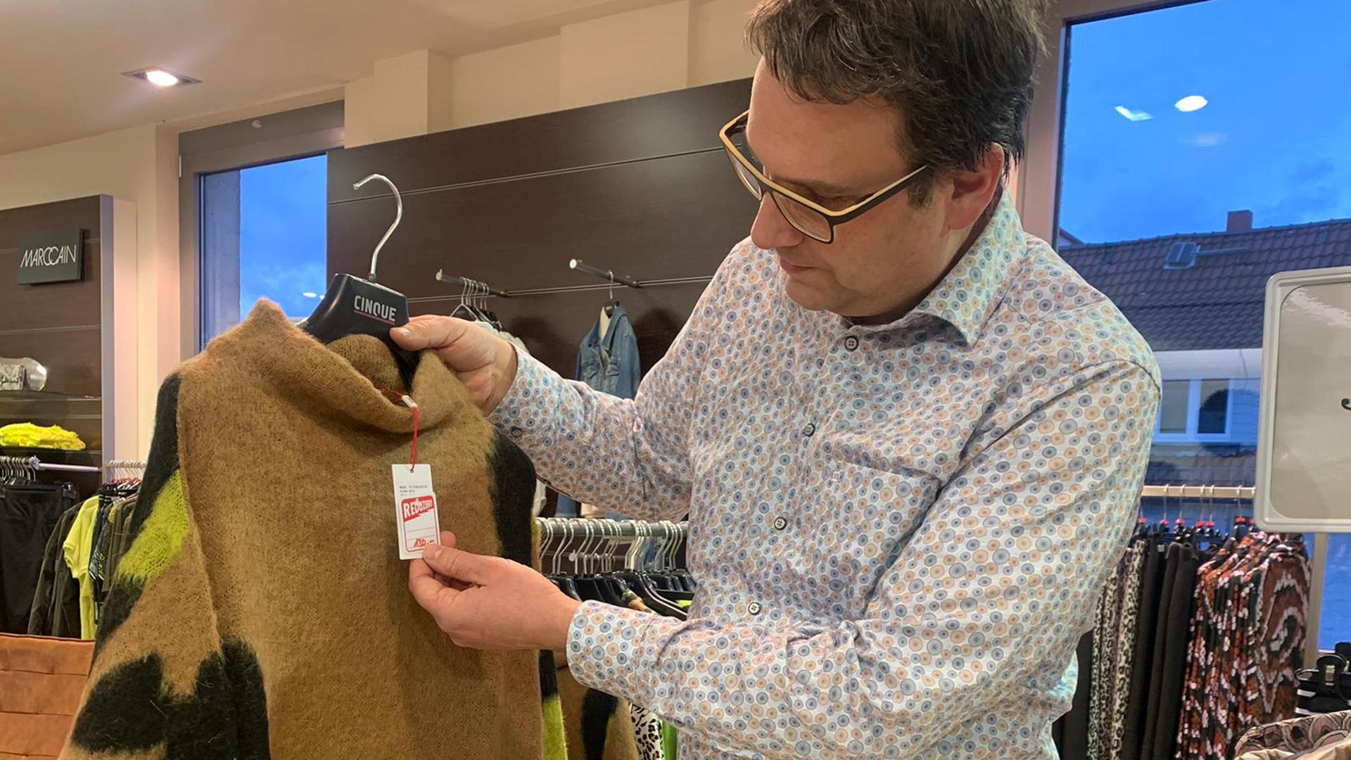 Ein Mann hält ein Kleidungsstück und schaut auf das Preisschild | HR