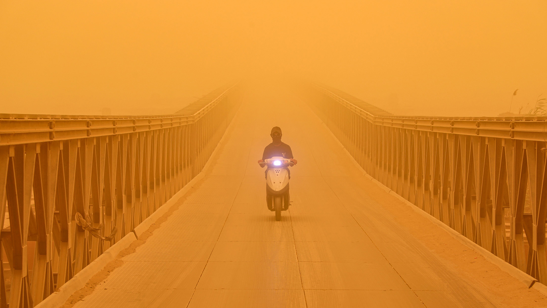 Ein Mann fährt inmitten eines heftigen Sandsturms im Irak mit einem Motorroller über eine Brücke. | AFP