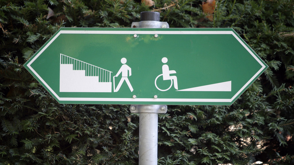 Ein Schild weist auf unterschiedliche Wege für Fußgänger und Rollstuhlfahrer hin