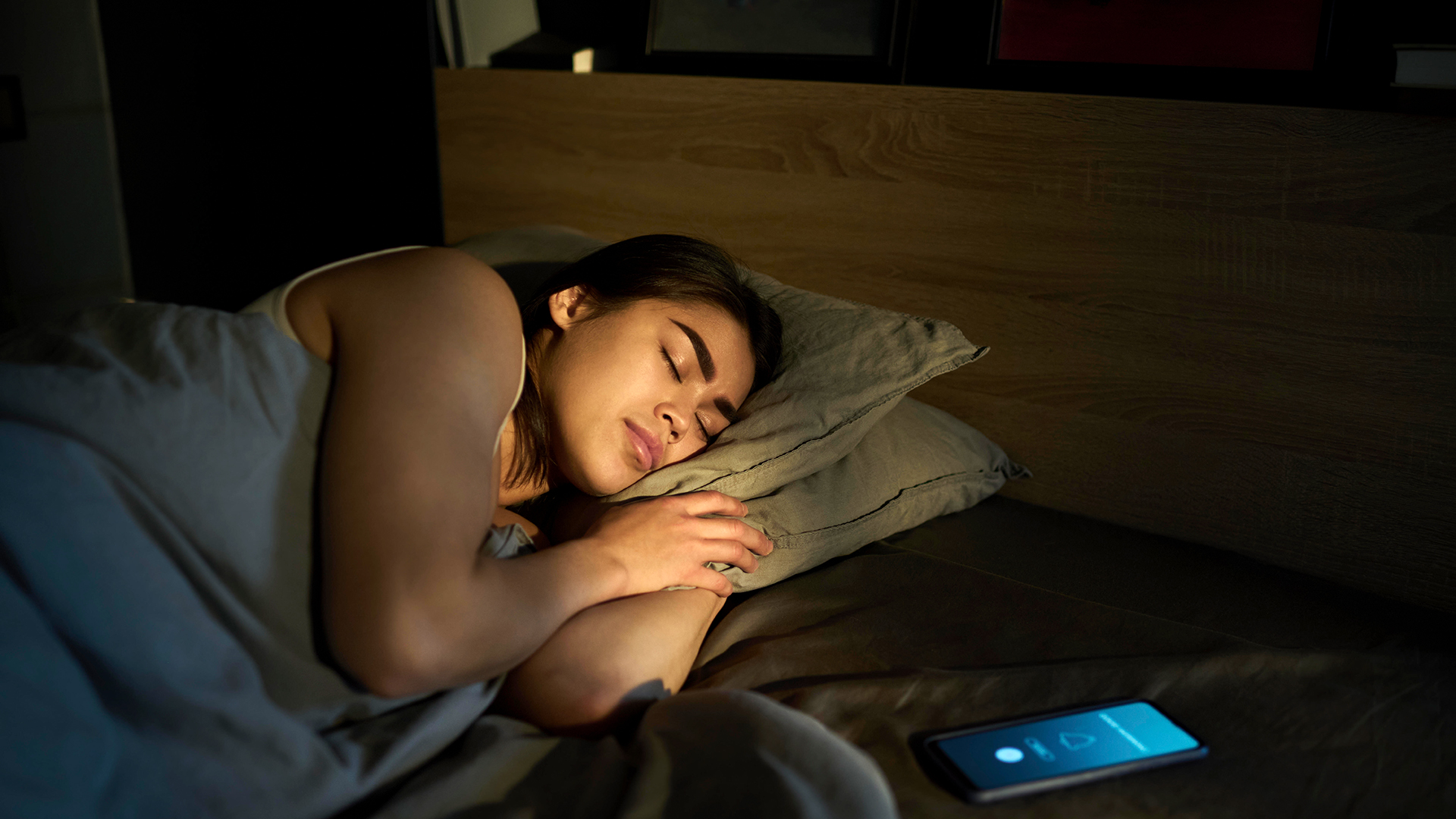Eine schlafende Frau, neben ihr liegt ein Mobiltelefon im Bett