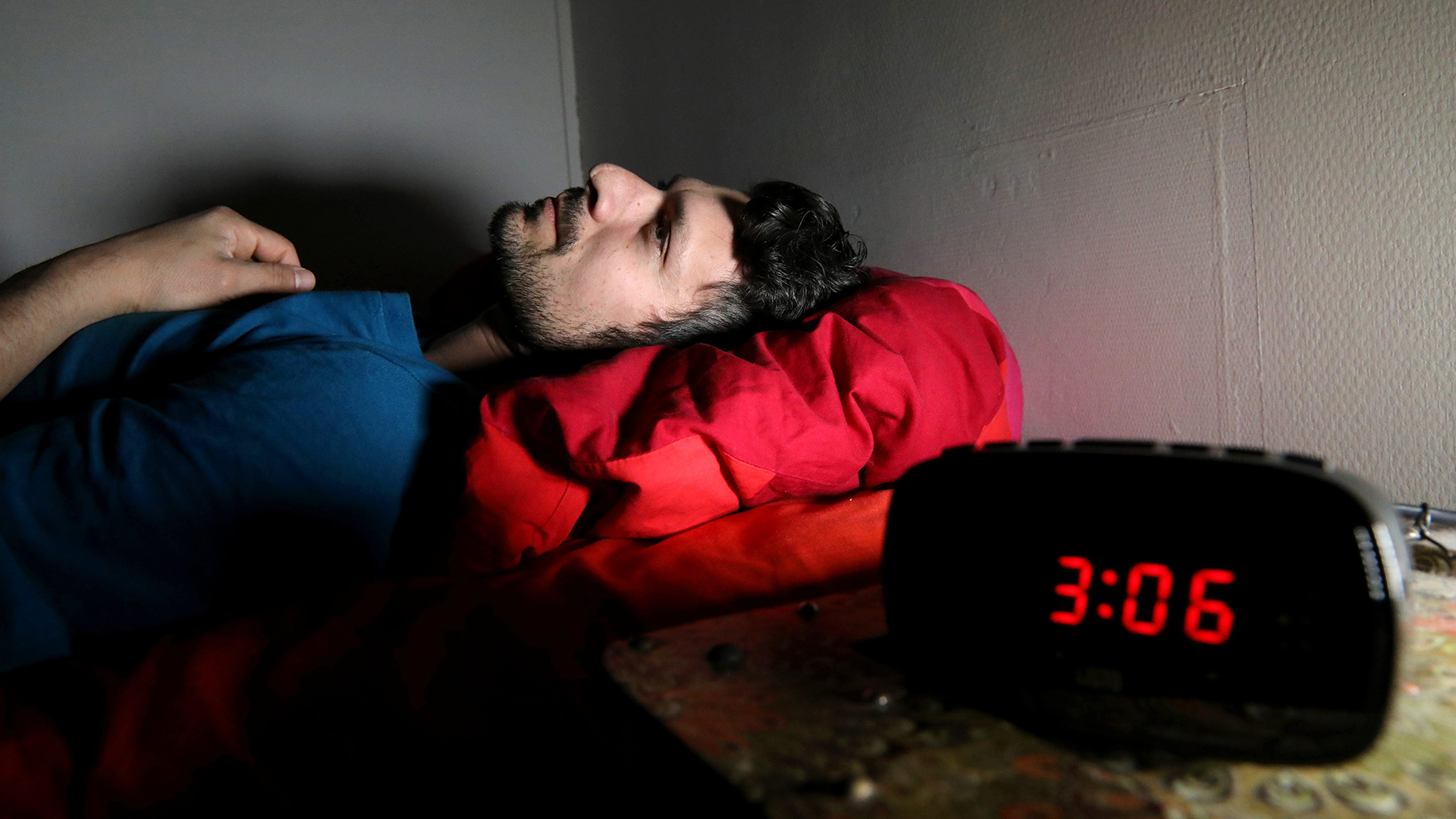 Ein Mann liegt im Bett - ein Digital-Wecker zeigt 03:06 Uhr. | picture alliance / PHOTOPQR/LA P